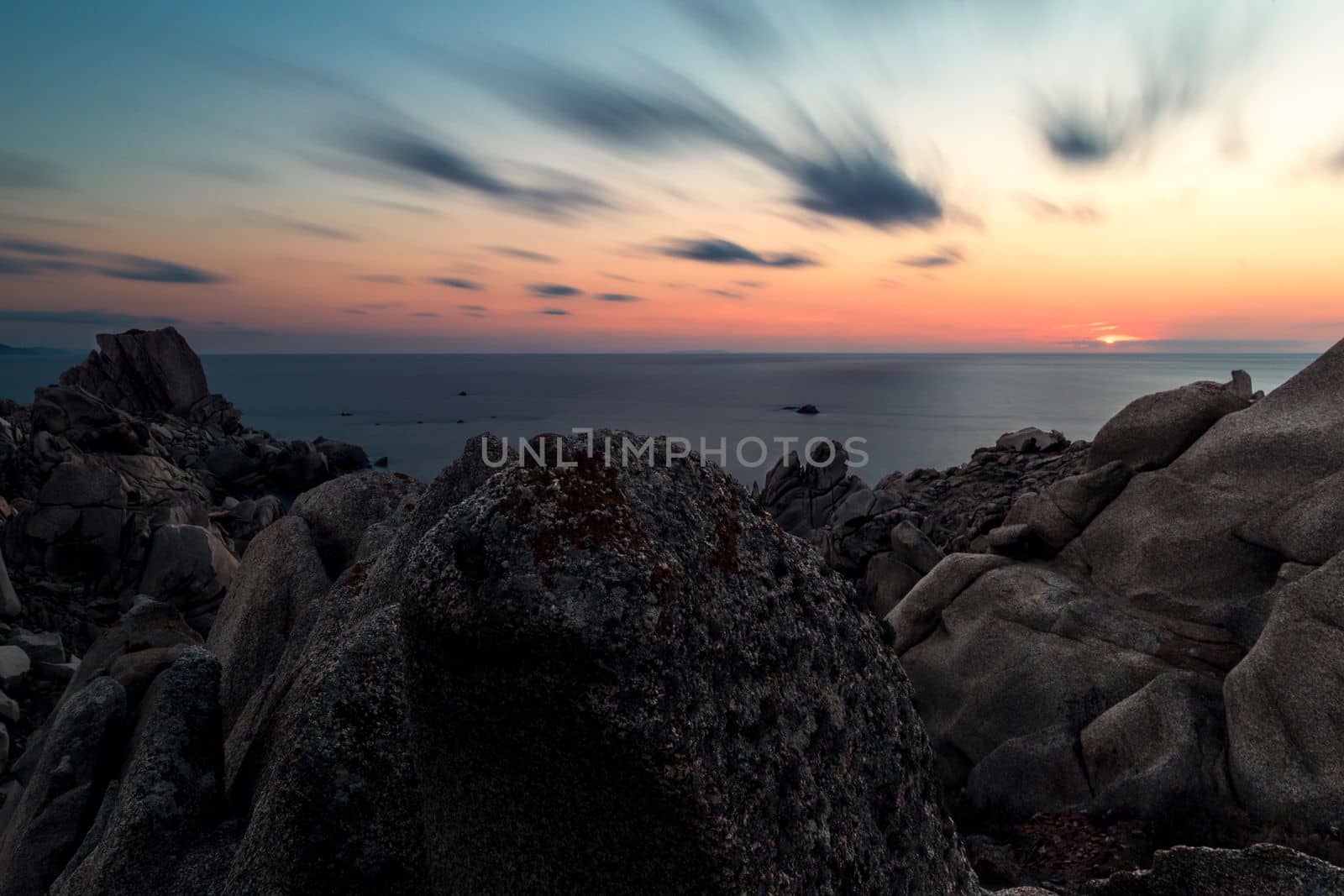 rocky coast seascape, sunset sun shines orange in the blue sky with few clouds, relaxing feeling of peace and tranquility. Long exposure. Capo Testa, Santa Teresa di Gallura, Sardinia, Italy