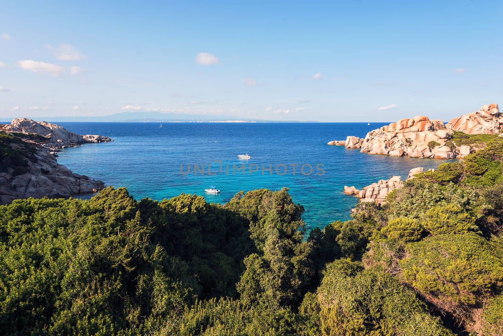 panoramic view of a cove with anchored boats. Vegetation and rocks surround it, scenic place for vacationers and summer holidays, bright colors. Capo Testa, Santa Teresa di Gallura, Sardinia, Italy