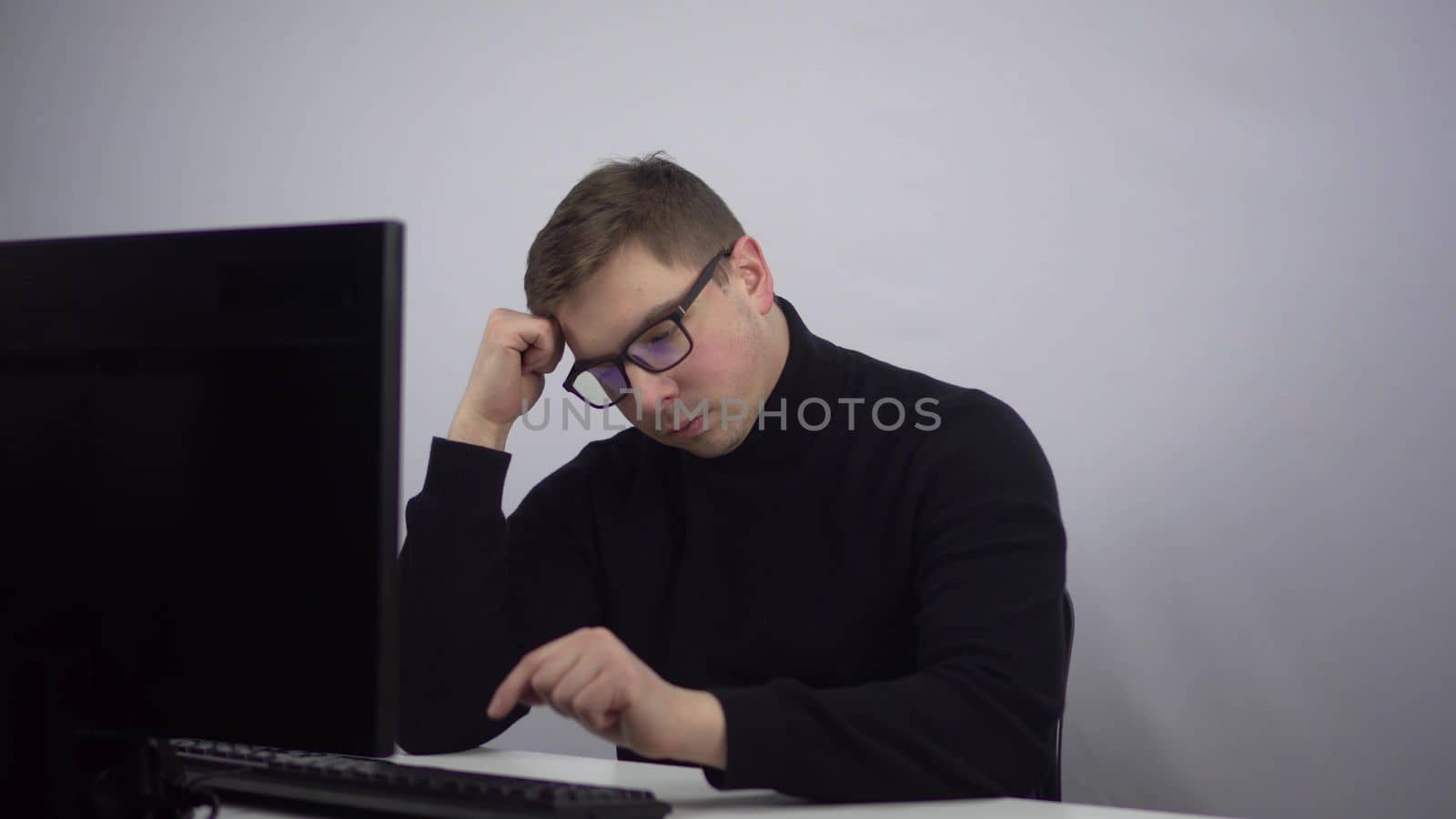 IT specialist lazily types on the computer. A young man with glasses sits in the office and works slowly. 4k