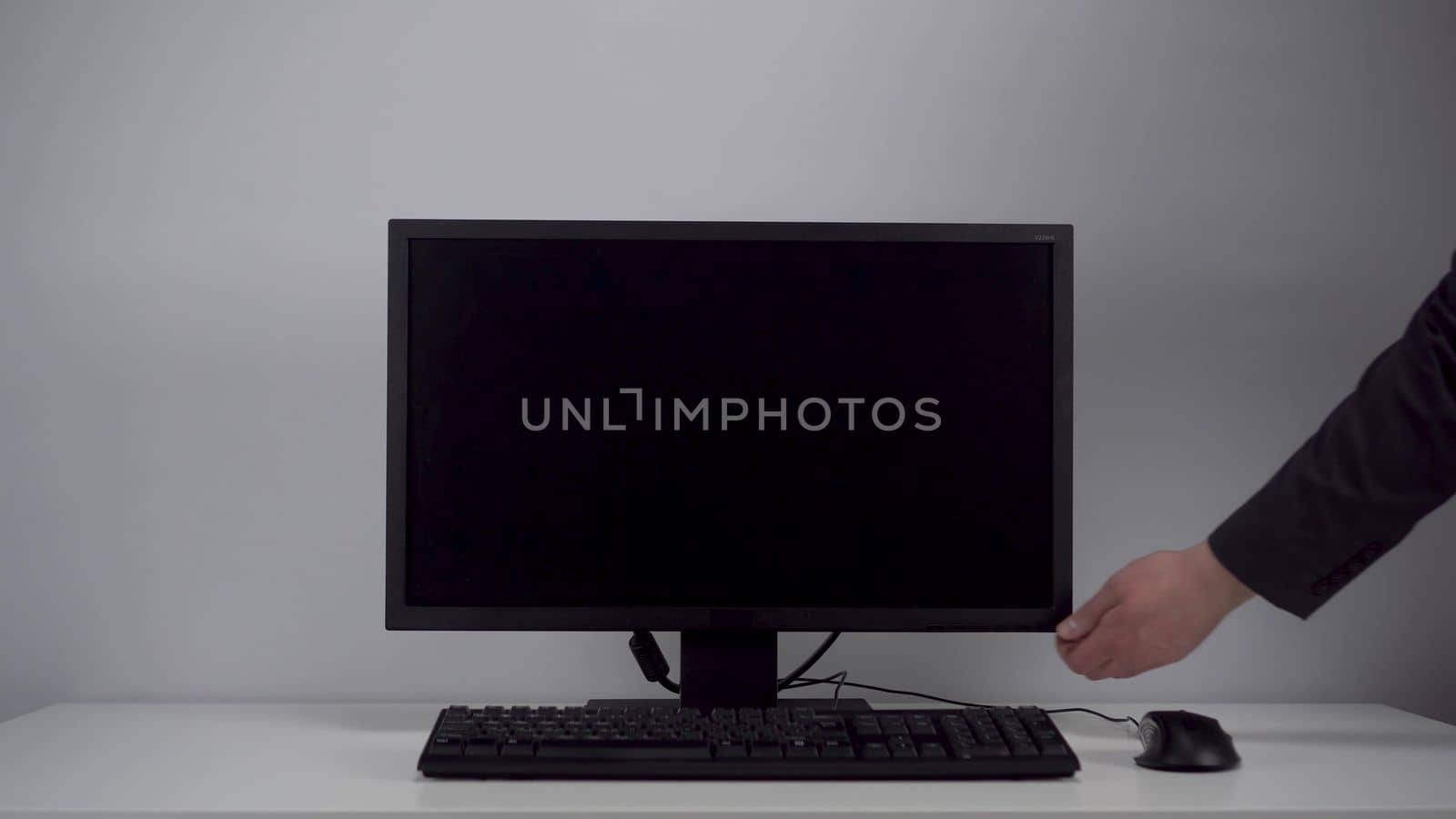 Turning on the monitor with a green screen. A man with his hand turns on the computer screen on the desktop in the office. Chroma key. 4k