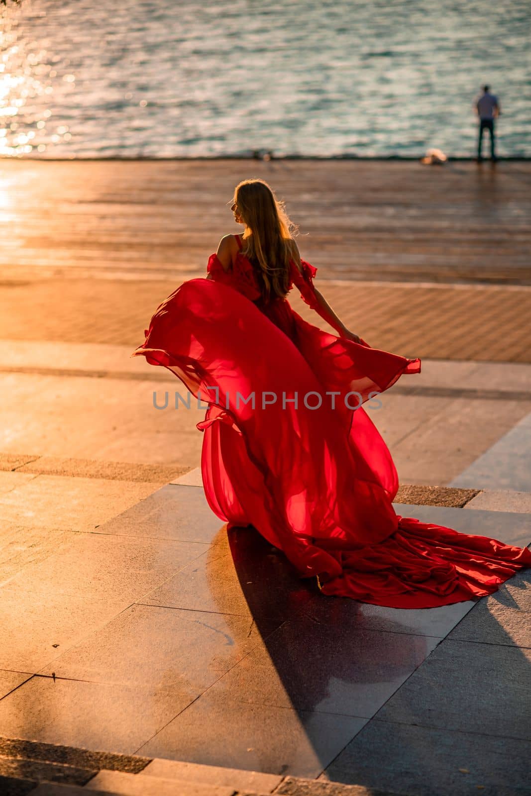 Sunrise red dress. A woman in a long red dress against the backdrop of sunrise, bright golden light of the sun's rays. The concept of femininity, harmony