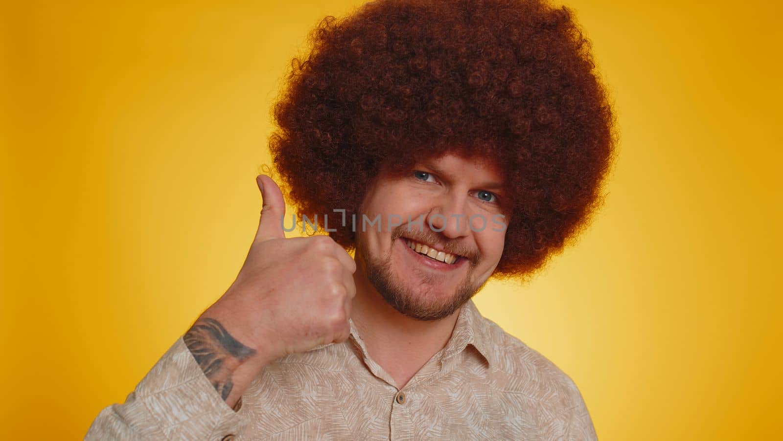 Like. Bearded man with lush Afro hairstyle coiffure raises thumbs up agrees with something, gives positive reply recommends advertisement likes good. Young hipster guy on yellow studio background