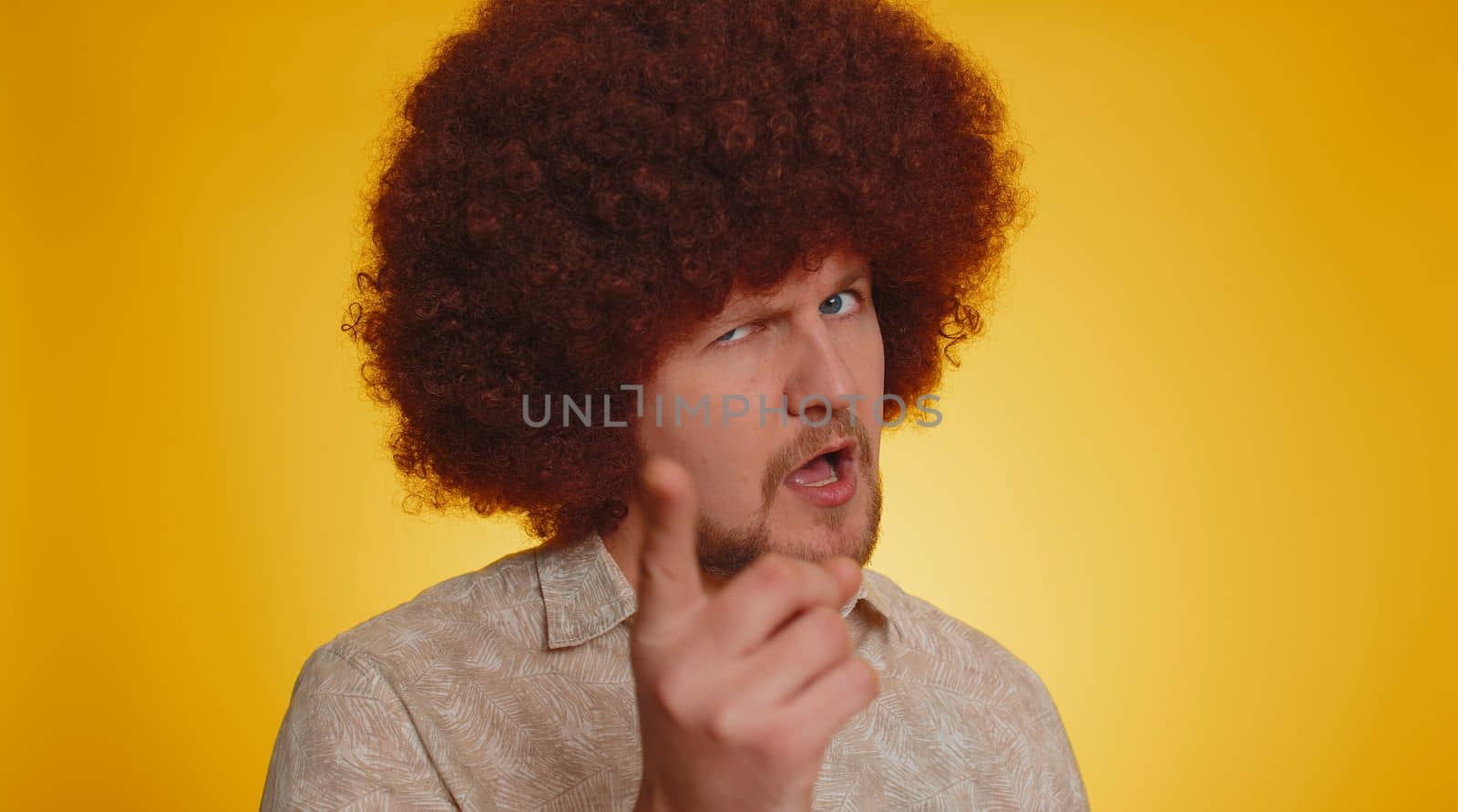 Bearded man with lush afro hairstyle coiffure shakes finger and saying no, be careful, scolding and giving advice to avoid danger mistake, disapproval sign. Hipster guy on yellow studio background