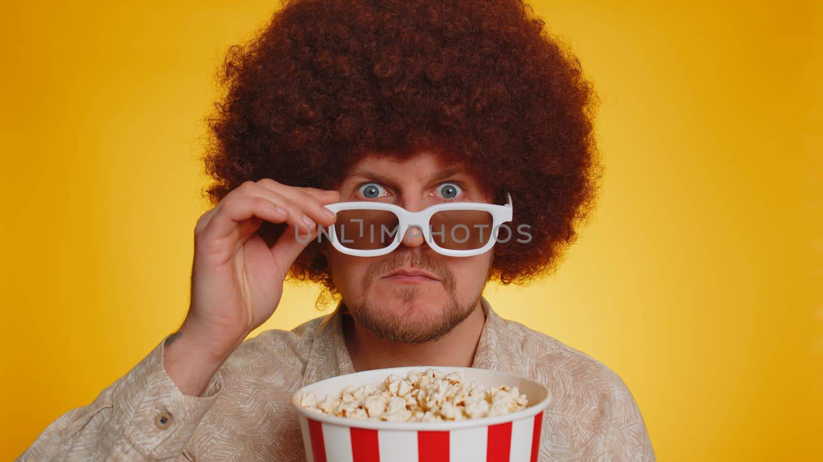 Excited bearded man with afro hairstyle eating popcorn and watching interesting tv serial, sport game, online social media movie film content. Hipster guy in 3D glasses enjoying domestic entertainment