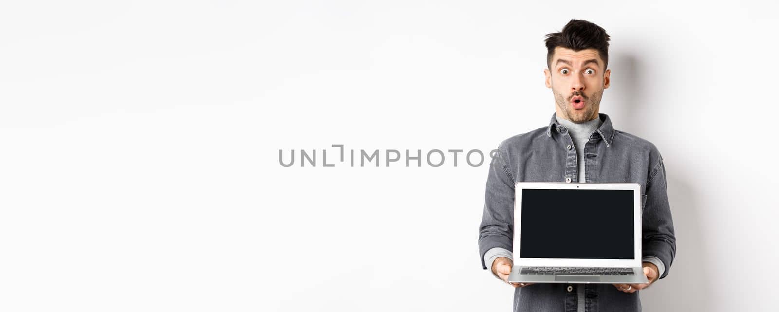 Excited man demostrated empty laptop screen, say wow and look at camera amazed, checking out online offer, showing webpage, standing on white background by Benzoix