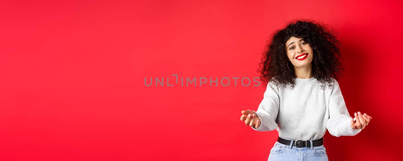 Pretty woman with curly haircut, extending hands and smiling with love and tenderness, inviting to come closer, reaching arms for hug, taking something into her arms, red background by Benzoix
