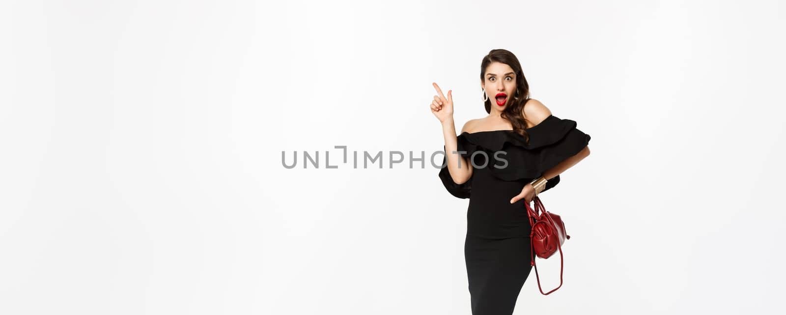 Beauty and fashion concept. Full length of excited young woman in glamour dress, red lips, having an idea, raising finger to suggest something, white background by Benzoix