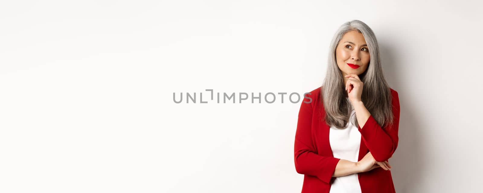 Business concept. Smiling mature lady in red blazer, smiling and looking satisfied while thinking, standing over white background by Benzoix