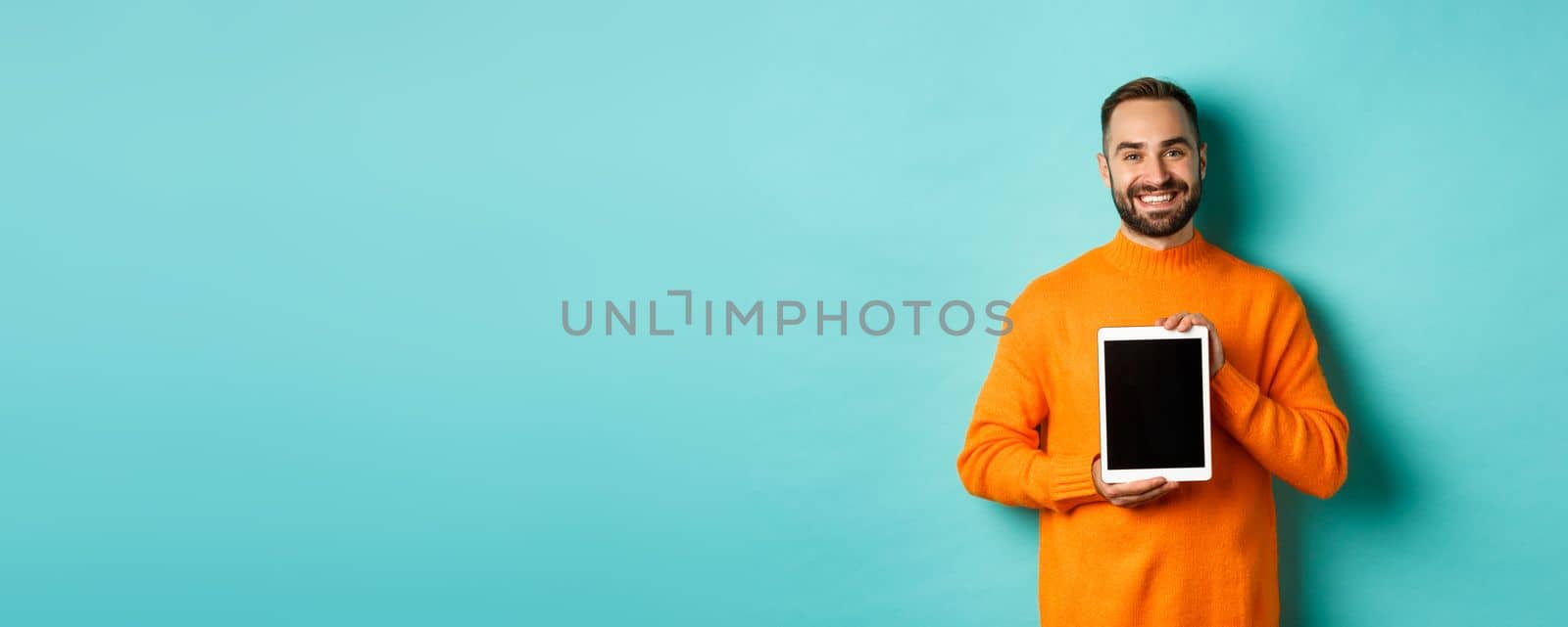 Technology. Smiling handsome man showing digital tablet screen, demonstrating application, standing over turquoise background by Benzoix