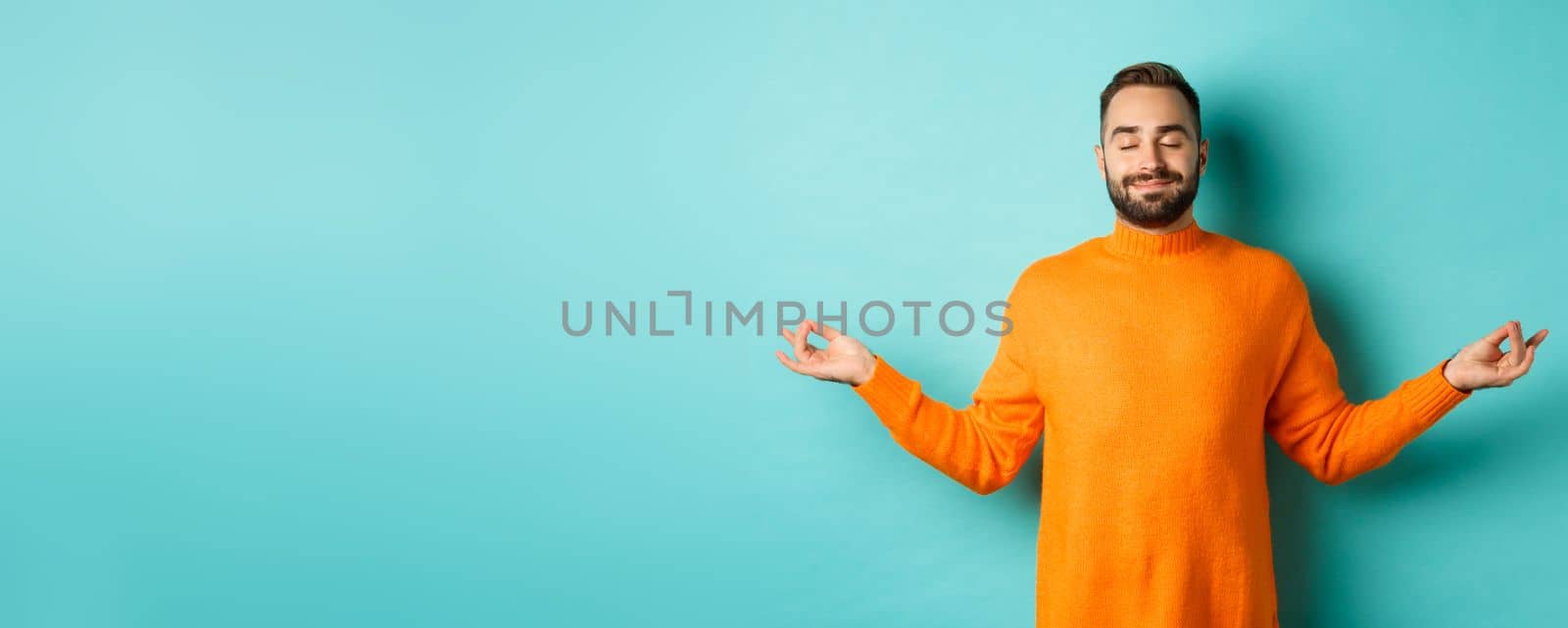 Image of relaxed and relieved man close eyes and smiling, feeling stress-free, meditating with calm expression, standing over light blue background.