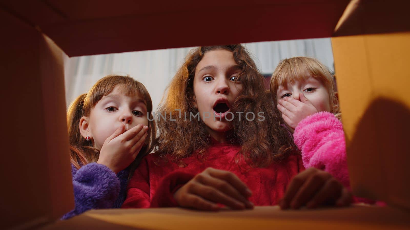 Three siblings children girls unpacking delivery parcel at home, inside viev from cardboard gift box by efuror