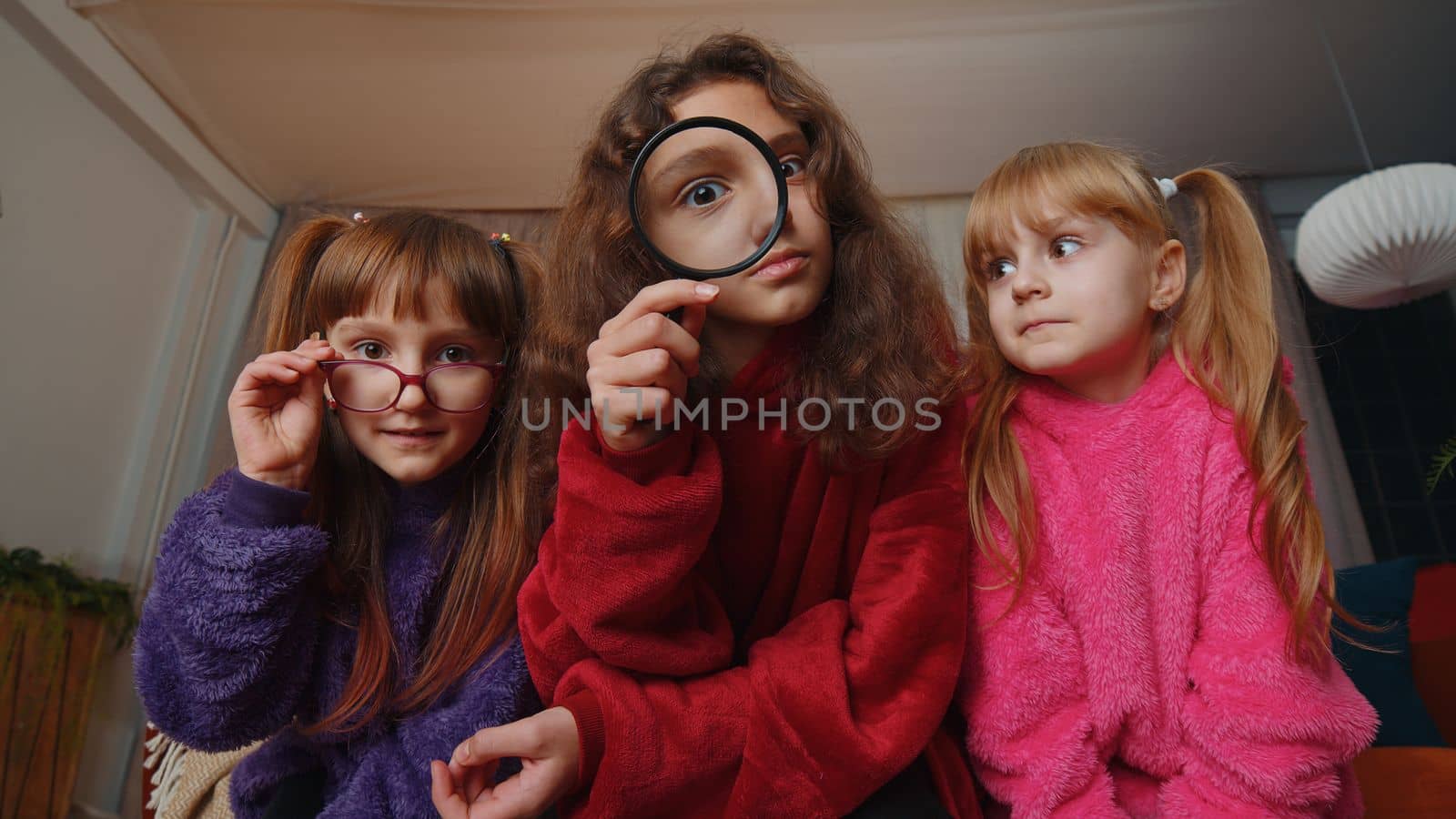 Children sisters girls holding magnifying glass near face, looking into camera, analysing, playing by efuror