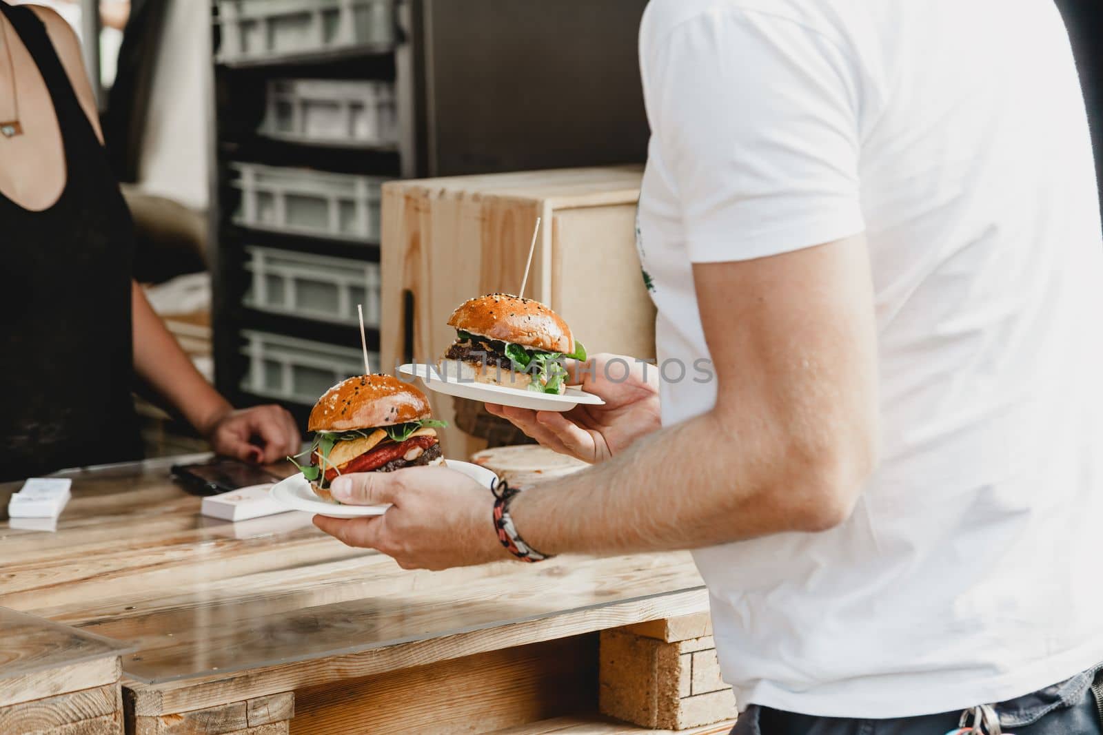 Man holds in his hand burgers at a burger feast. Dinner Hamburger Food Feast Party. Big burger in hands at street food outdoor festival. Festival food day.