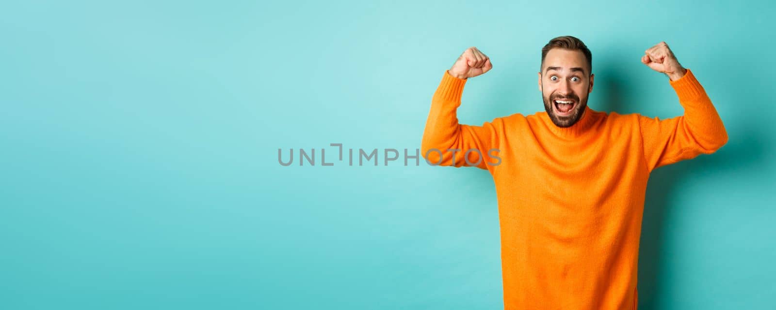 Handsome man celebrating victory, winning and looking happy, triumphing over win, standing over light blue background.