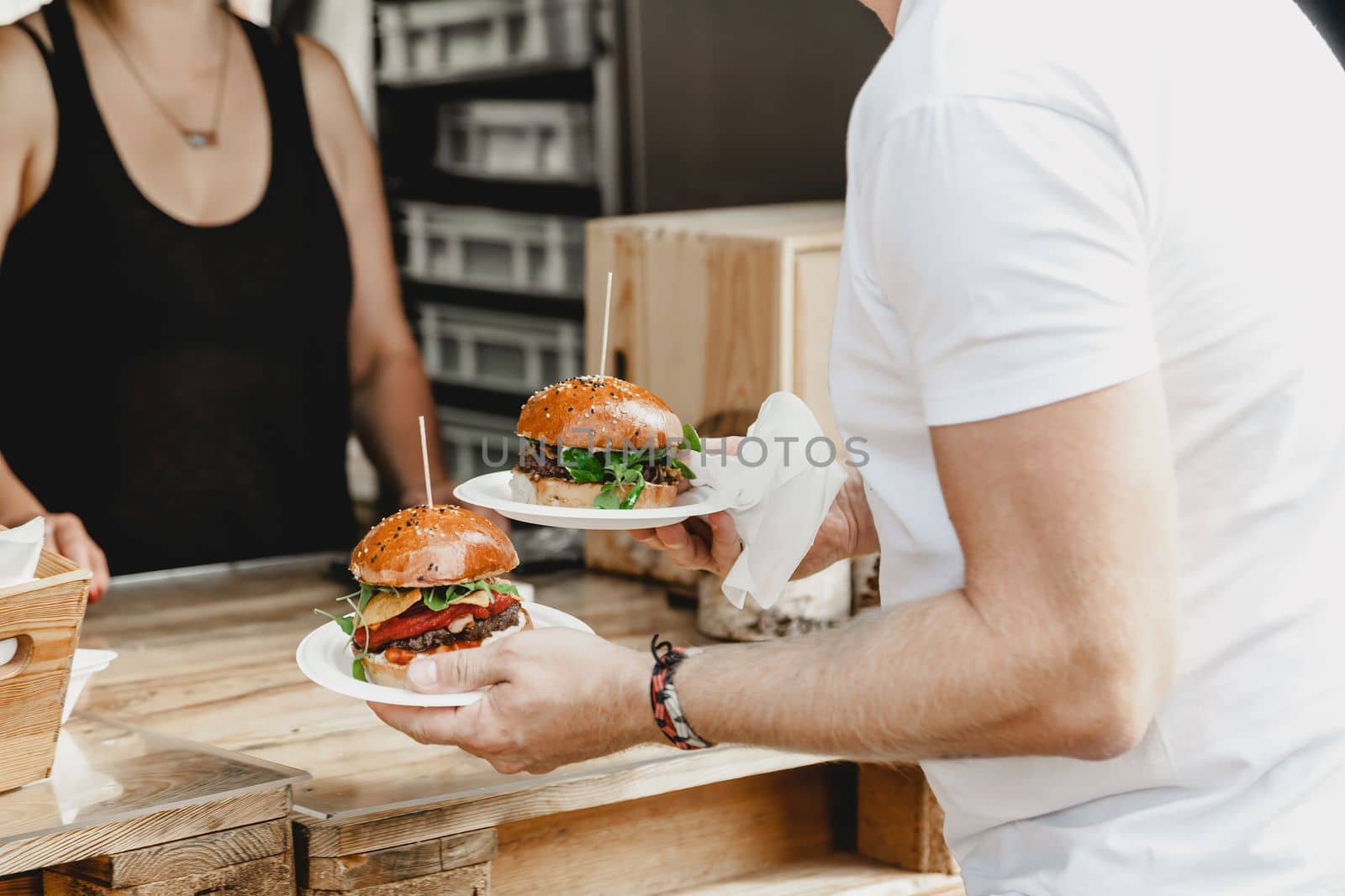 Man holds in his hand burgers at a burger feast. Dinner Hamburger Food Feast Party. Big burger in hands at street food outdoor festival. Festival food day.