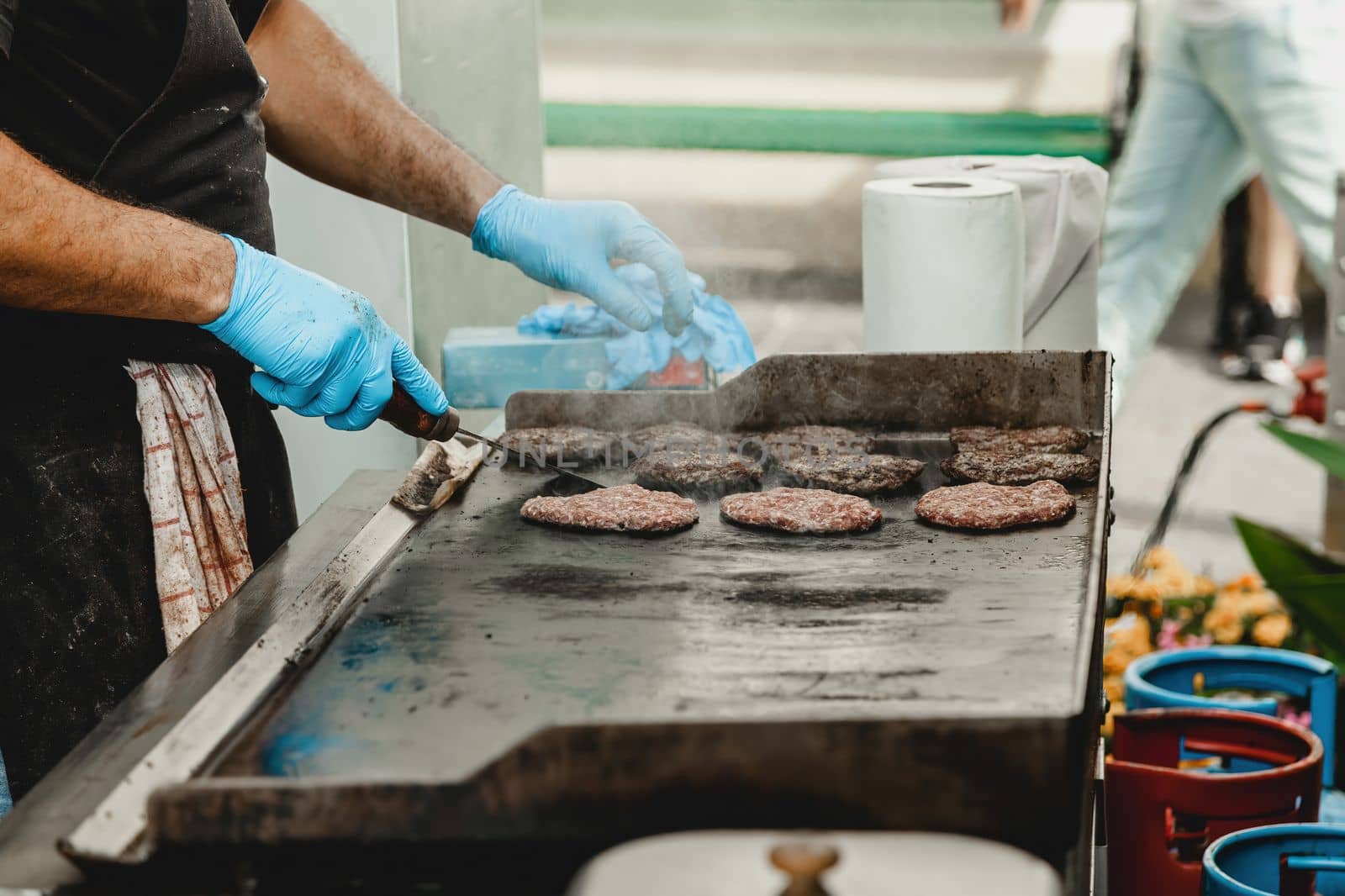 A man fries burger meatballs. Man grills some kind of marinated meat on gas grill during summer time. Meat on the grill is cooked by man's hand in a blue glove