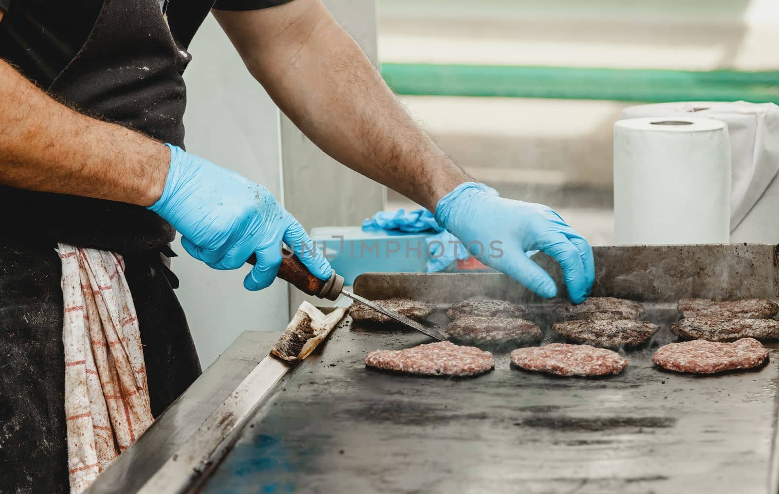 A man fries burger meatballs. Man grills some kind of marinated meat on gas grill during summer time. Meat on the grill is cooked by man's hand in a blue glove