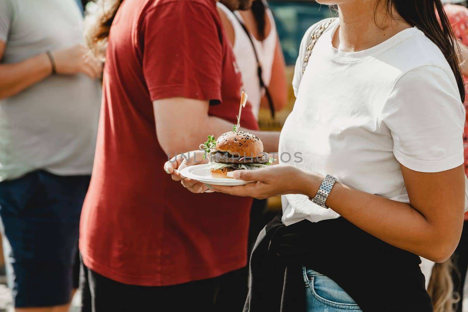 Woman holds in his hand burgers at a burger feast. Dinner Hamburger Food Feast Party. Big burger in hands at street food outdoor festival. Festival food day.