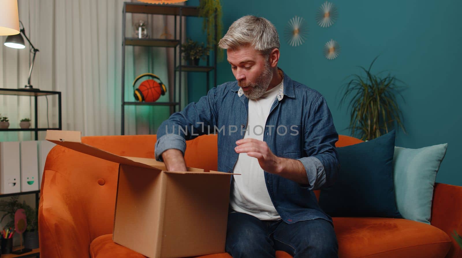 Happy surprised winner man unpacking delivery parcel at home. Smiling satisfied mature guy shopper online shop customer opening cardboard box receiving purchase gift headphones by fast postal shipping