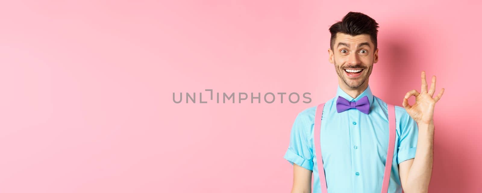 Handsome caucasian man with moustache smiling and showing okay sign, approve something good, praising excellent choice, standing amused on pink background by Benzoix