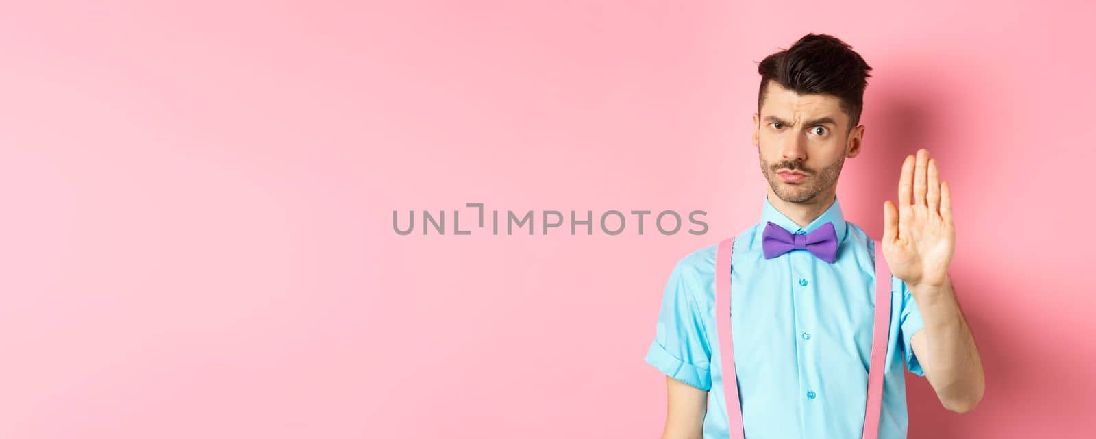 Serious-looking man prohibit something bad, stretch out hand to stop you, forbid action, saying no and looking strict, standing over pink background.