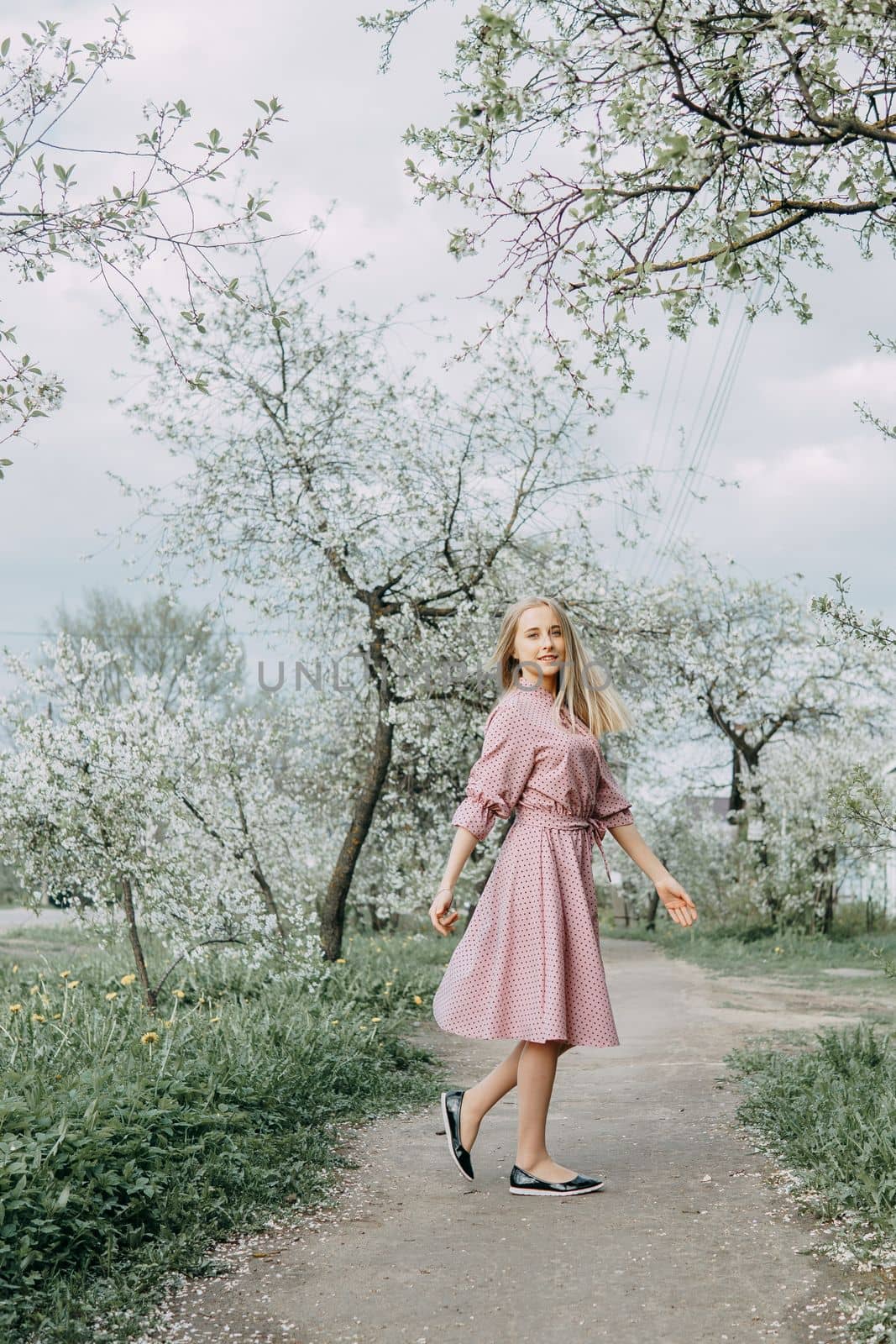 Blonde girl on a spring walk in the garden with cherry blossoms. Female portrait, close-up. A girl in a pink polka dot dress. by Annu1tochka