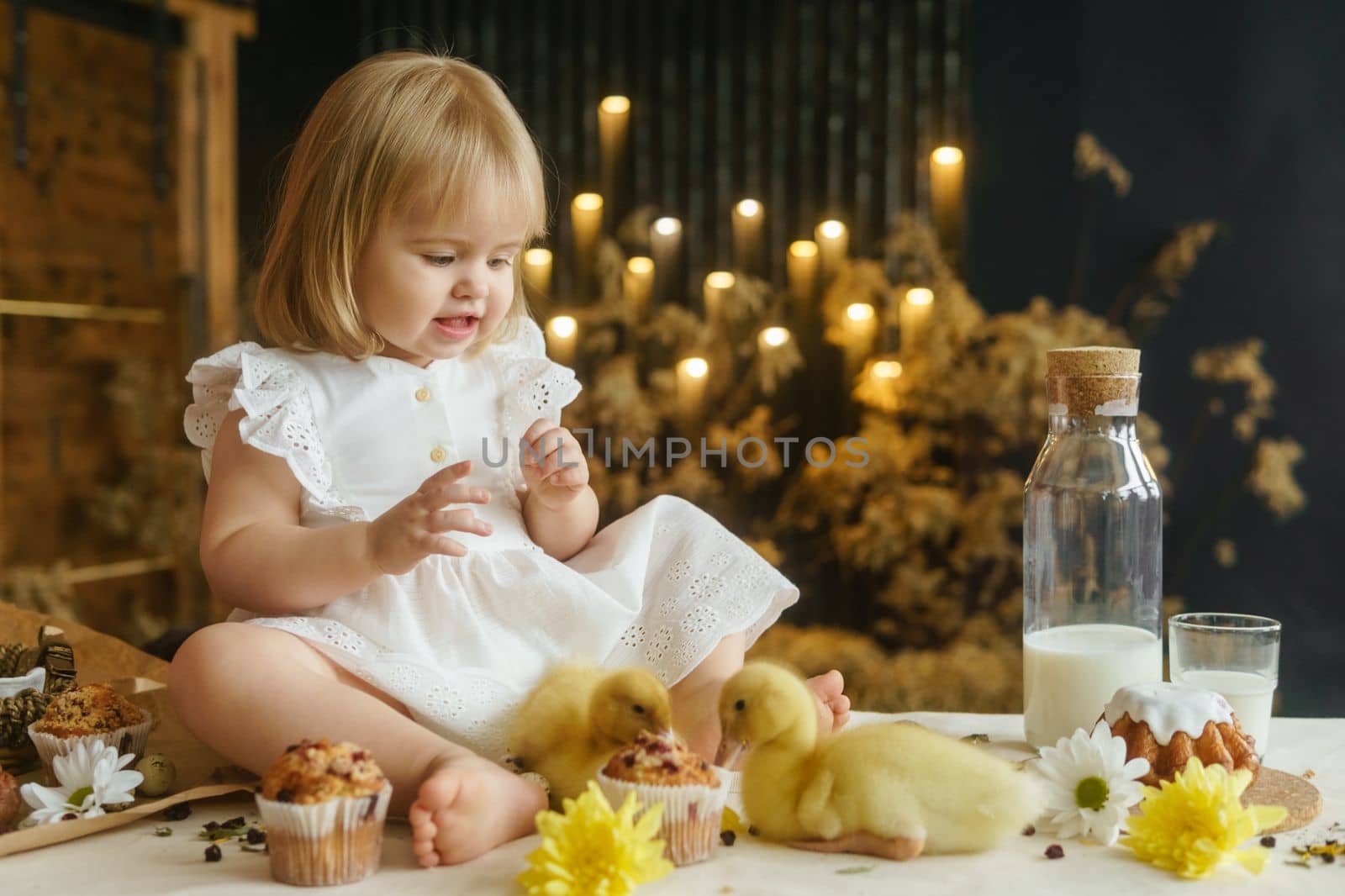 A little girl is sitting on the Easter table and playing with cute fluffy ducklings. The concept of celebrating happy Easter