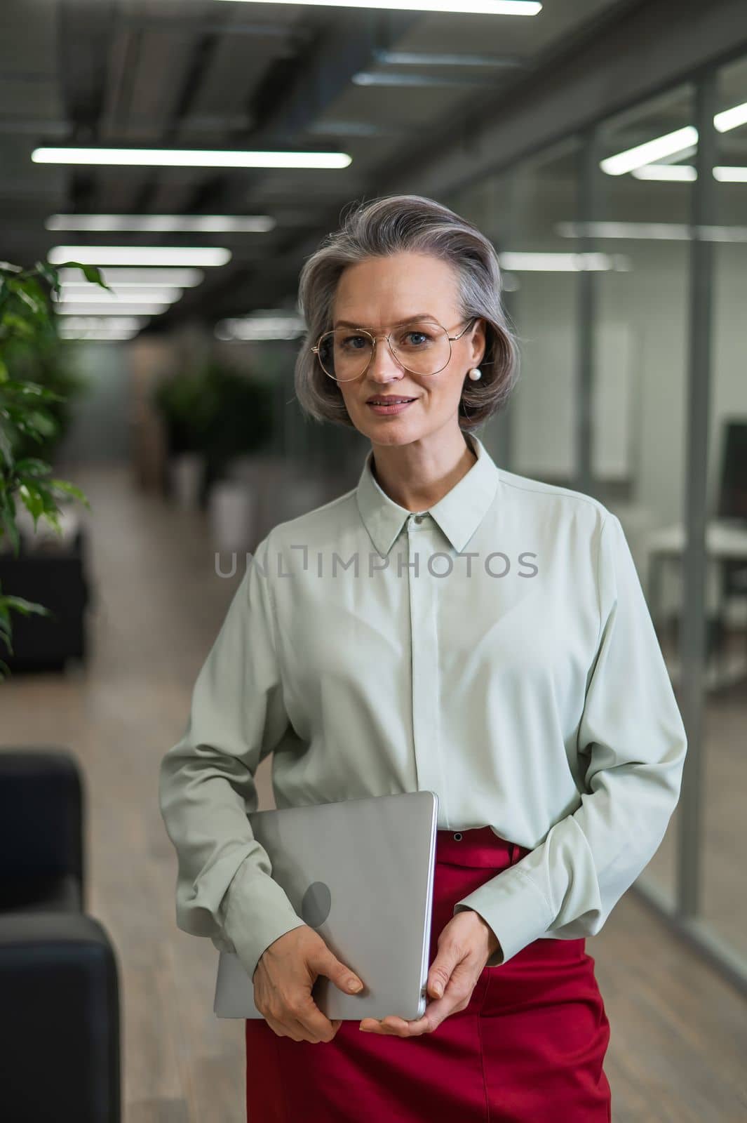 Mature caucasian woman stands with a laptop among the office. by mrwed54