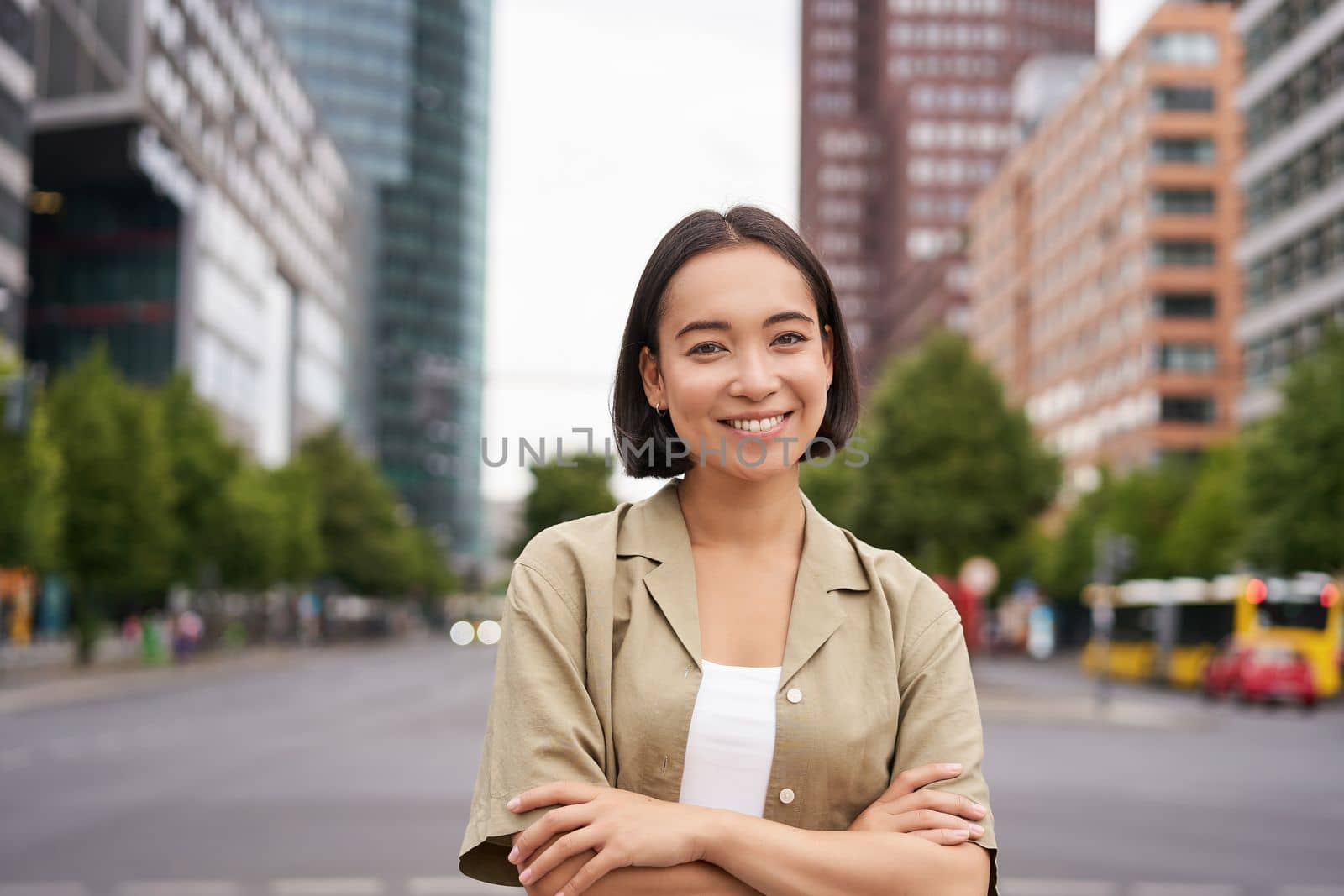 Urban people. Young happy asian girl cross arms on chest, posing on busy city street, smiling with confidence at camera by Benzoix