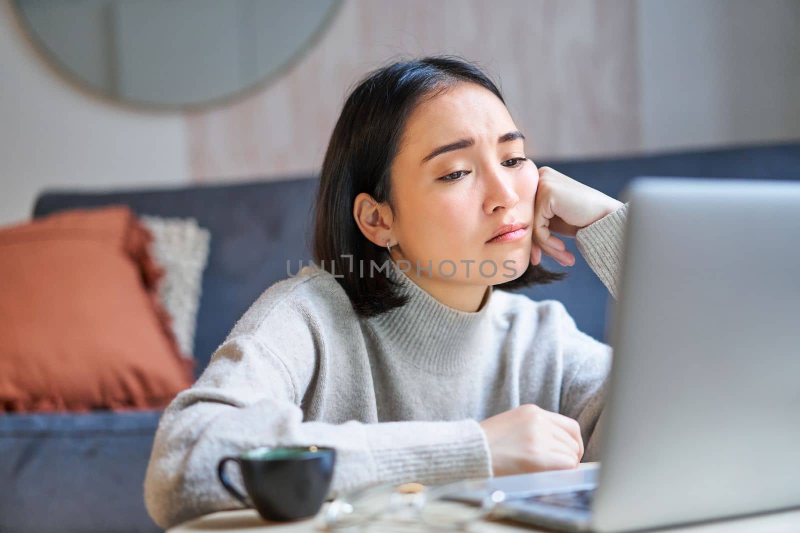 Portrait of korean girl sits bored, student looks gloomy at laptop, sitting at home and expressing boredom.