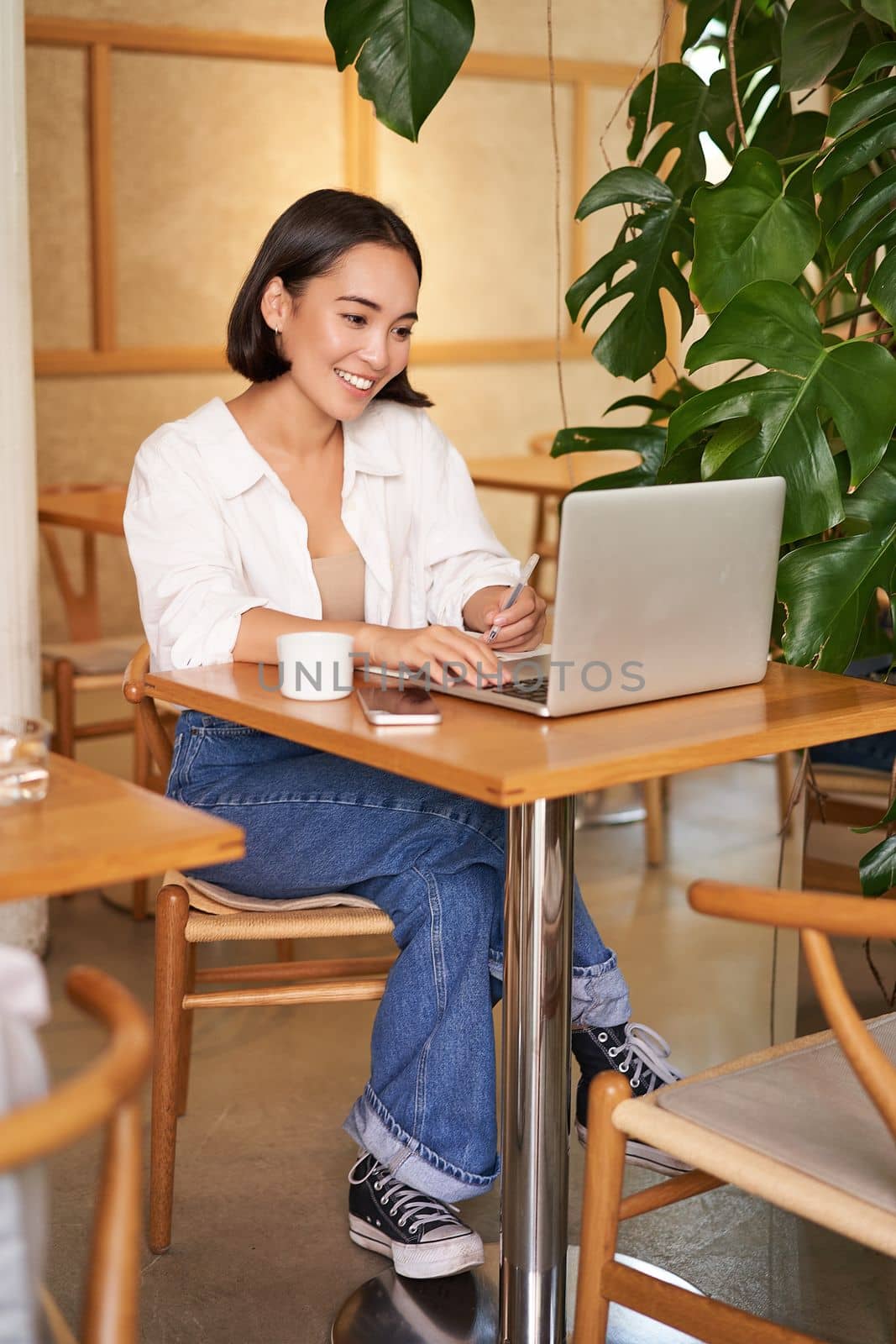 Stylish businesswoman with laptop, sitting in cafe and working on computer, managing business and drinking coffee by Benzoix