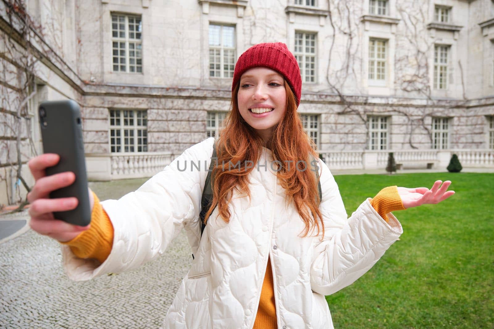 Portrait of happy tourist, girl with backpack, video chats, shows building, sightseeing attraction to friend, poses near landmark and smiles by Benzoix