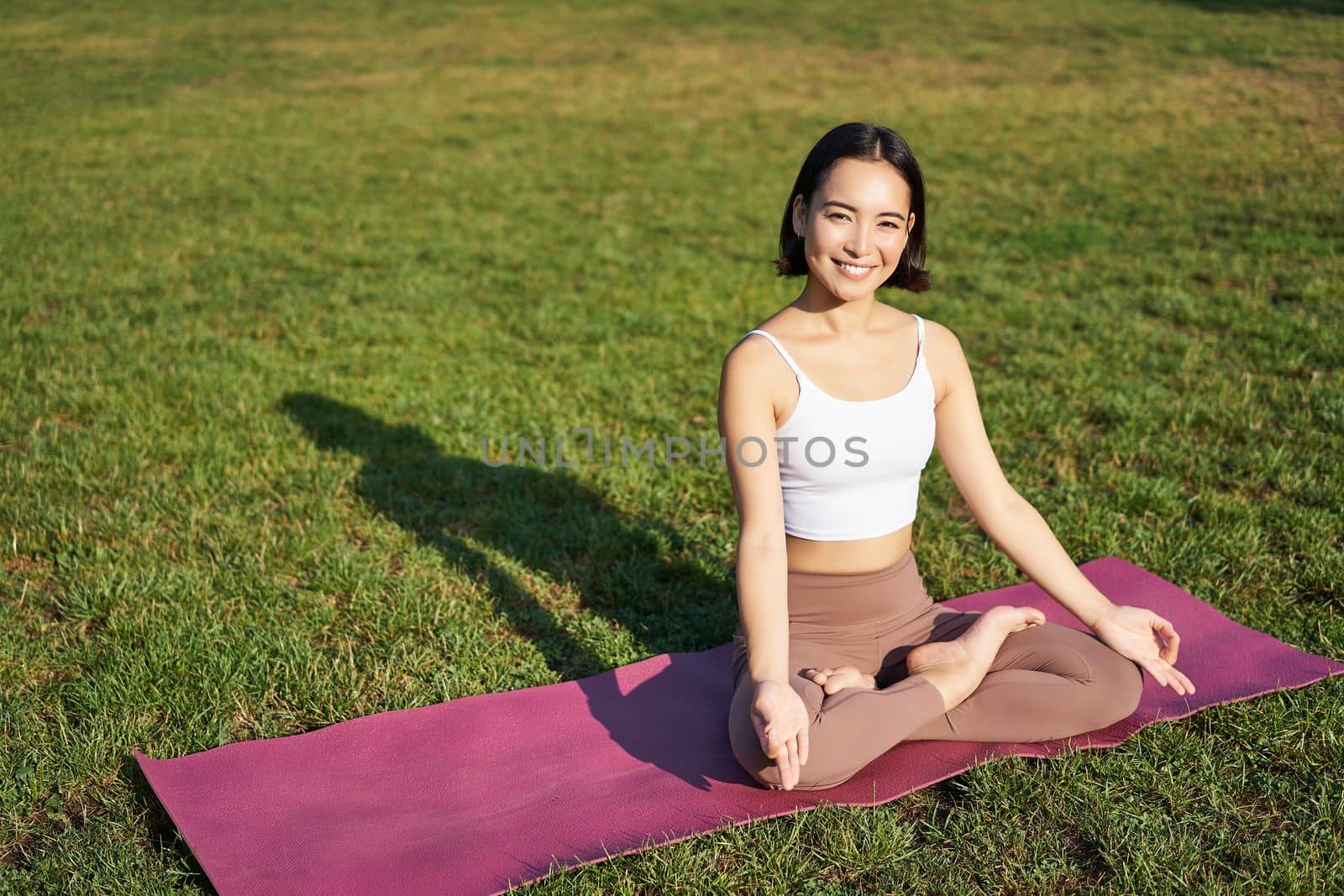 Mindfulness and meditation. Young asian woman smiling while doing yoga, relaxing in asana on rubber mat, doing exercises in park on fresh air.