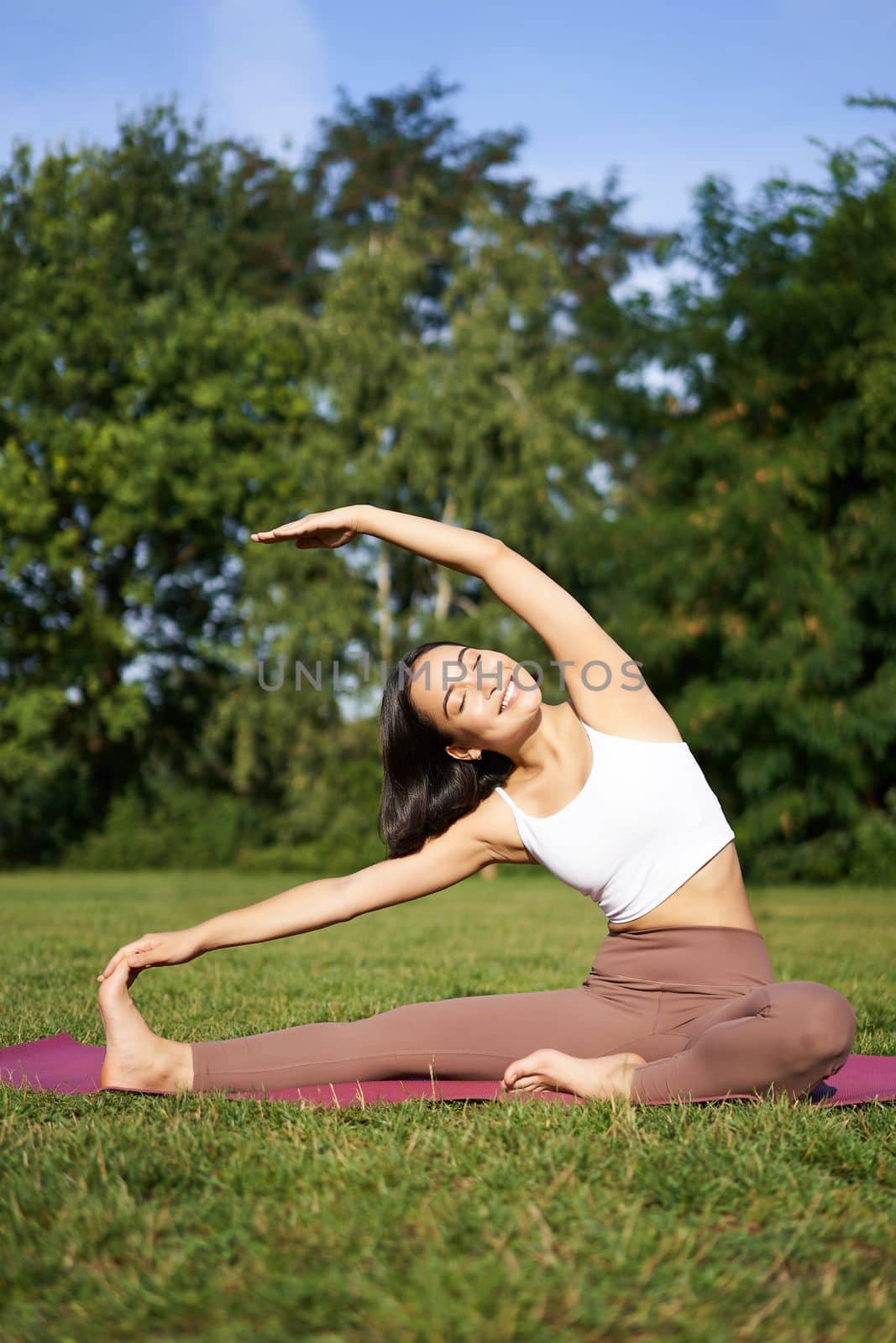 Young woman does yoga on lawn in park, stretching on fitness mat, wellbeing concept by Benzoix