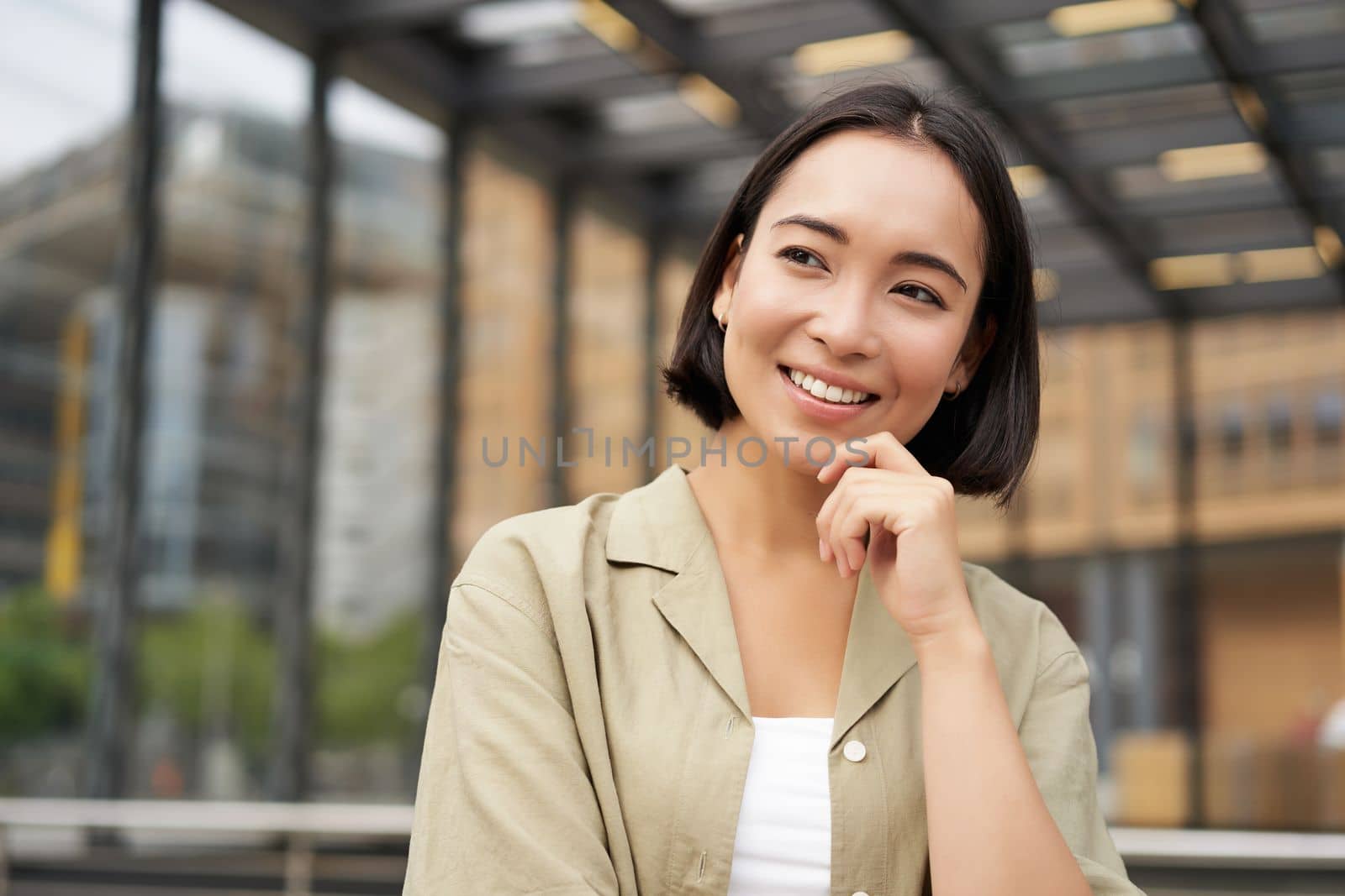 Portrait of beautiful young woman in casual clothes, smiling, posing outdoors on an empty street near glass building.