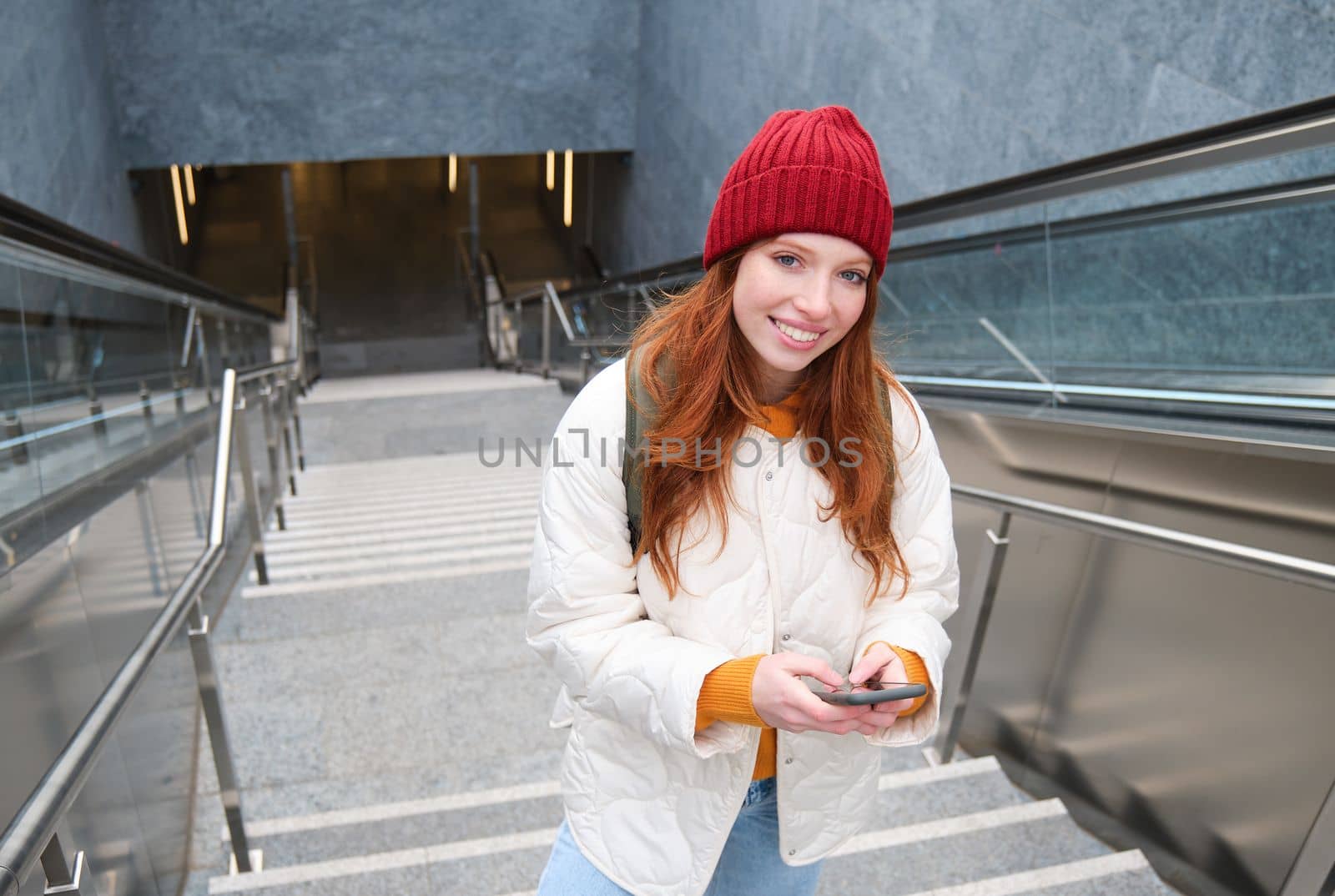 Smiling girl walking on stairs, using mobile phone, texting message on her way, using smartphone app map, follows route to destination place by Benzoix