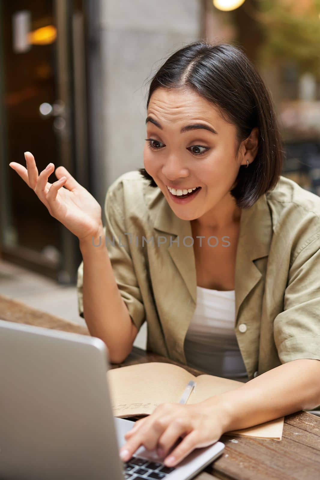 Vertical shot of young brunette girl chatting on video chat, having online meeting, talking to laptop, sitting in cafe.