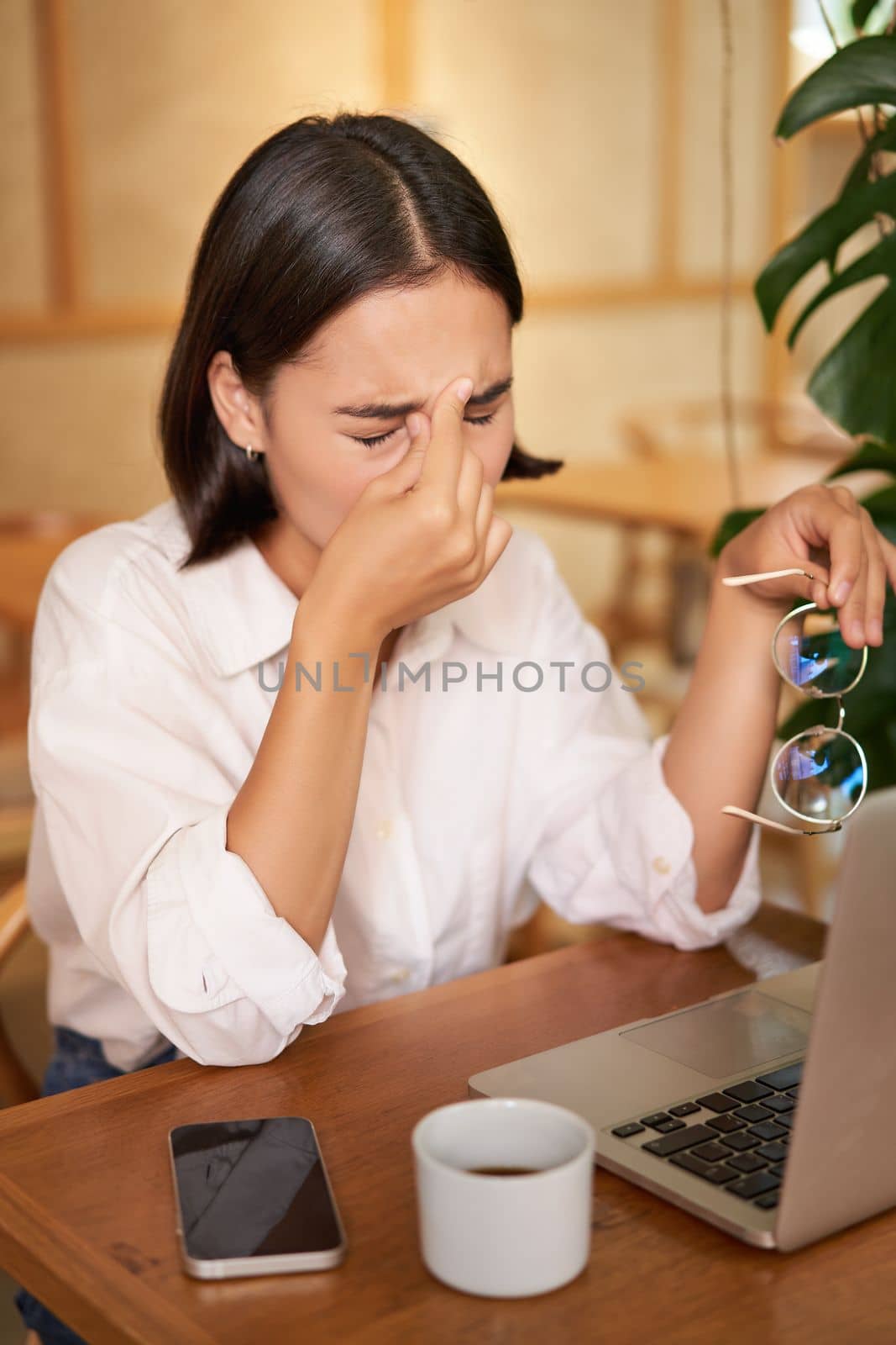 Working woman feeling tired, rubbing eyes after using laptop, having fatigue, sitting in cafe with coffee.