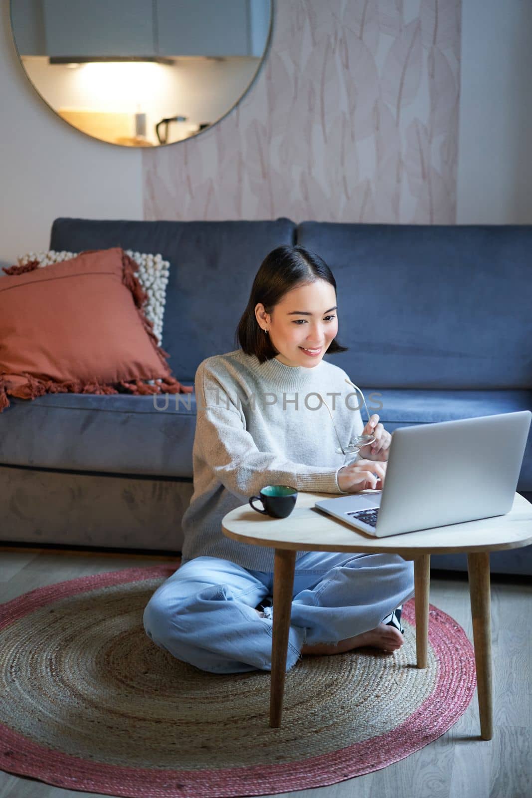 Vertical shot of asian girl sits on floor at home, working on laptop, studying at cozy place, using computer to freelance.