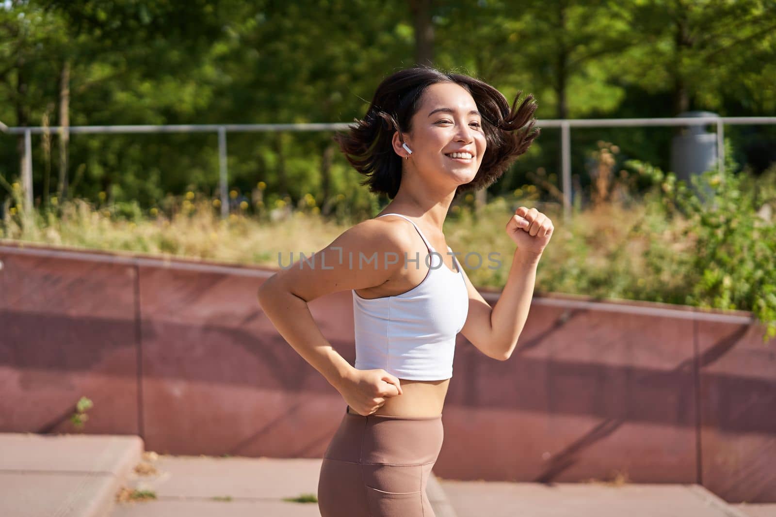 Wellbeing. Smiling asian fitness girl, runner in park, smiling and running, doing jogging workout outdoors on streets by Benzoix