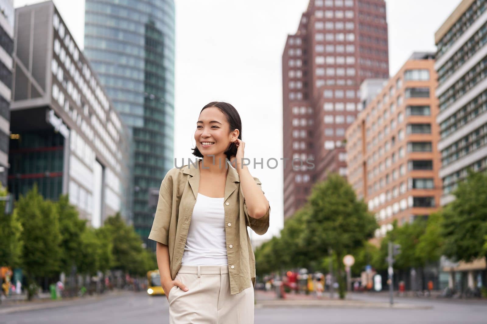 Outdoor shot of young smiling asian woman, standing on street in daytime, looking around, posing happy by Benzoix