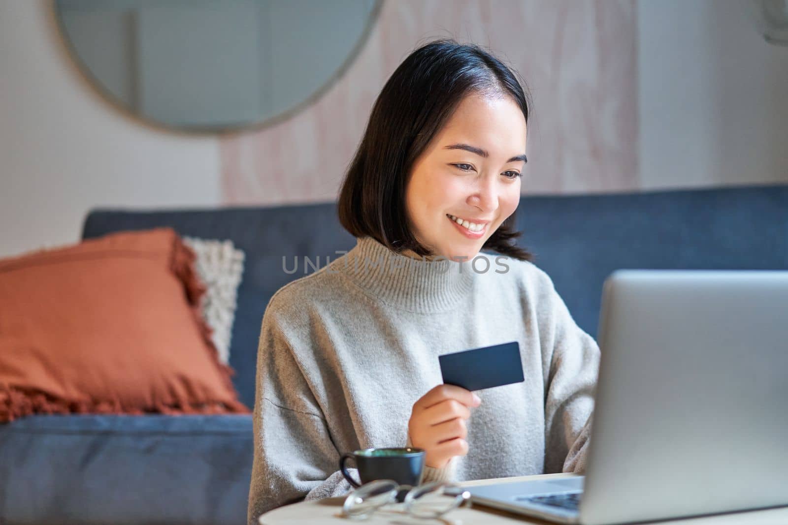 Portrait of korean woman shopping online, using her credit card and laptop to order delivery from website.