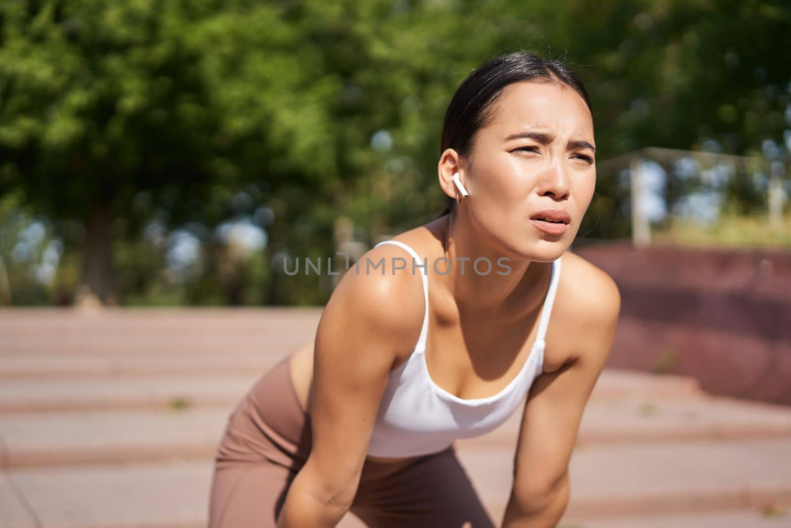 Tired young female runner, asian girl taking break during workout, stop jogging, panting while breathing, running in park by Benzoix