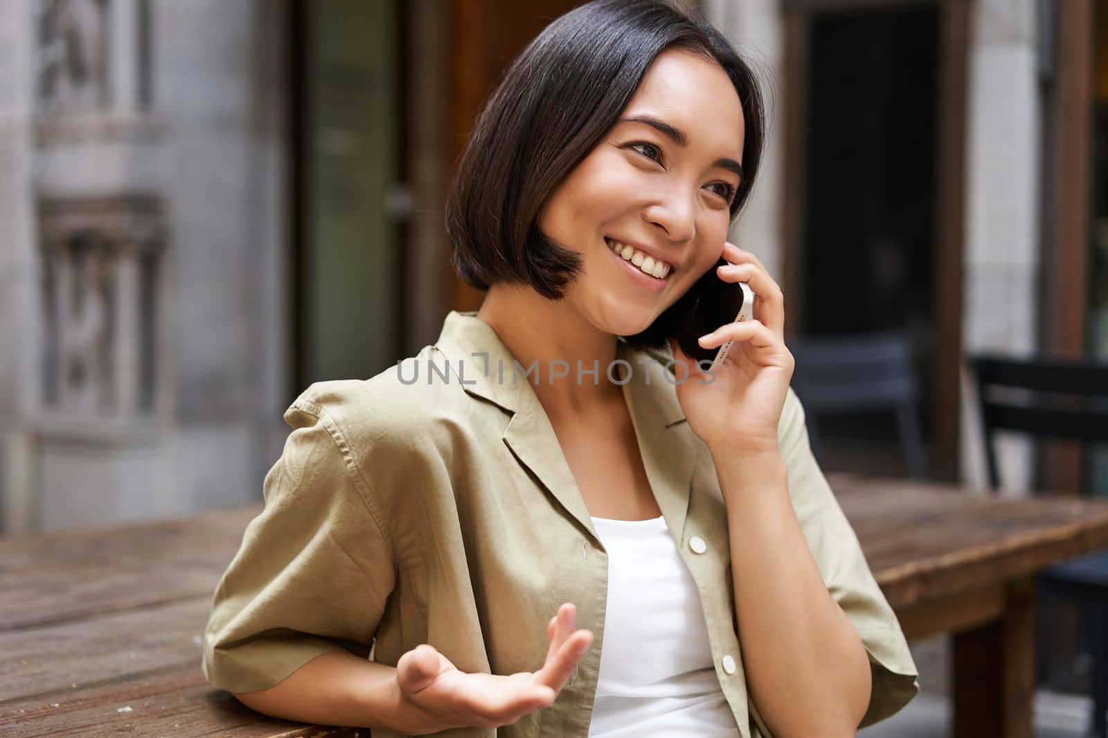 Young woman having conversation on mobile phone, sitting outdoors and making phone call, using smartphone, talking.