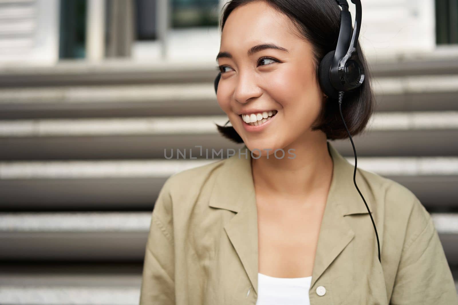Portrait of beautiful girl in earphones, listening music, smiling and walking in city centre.