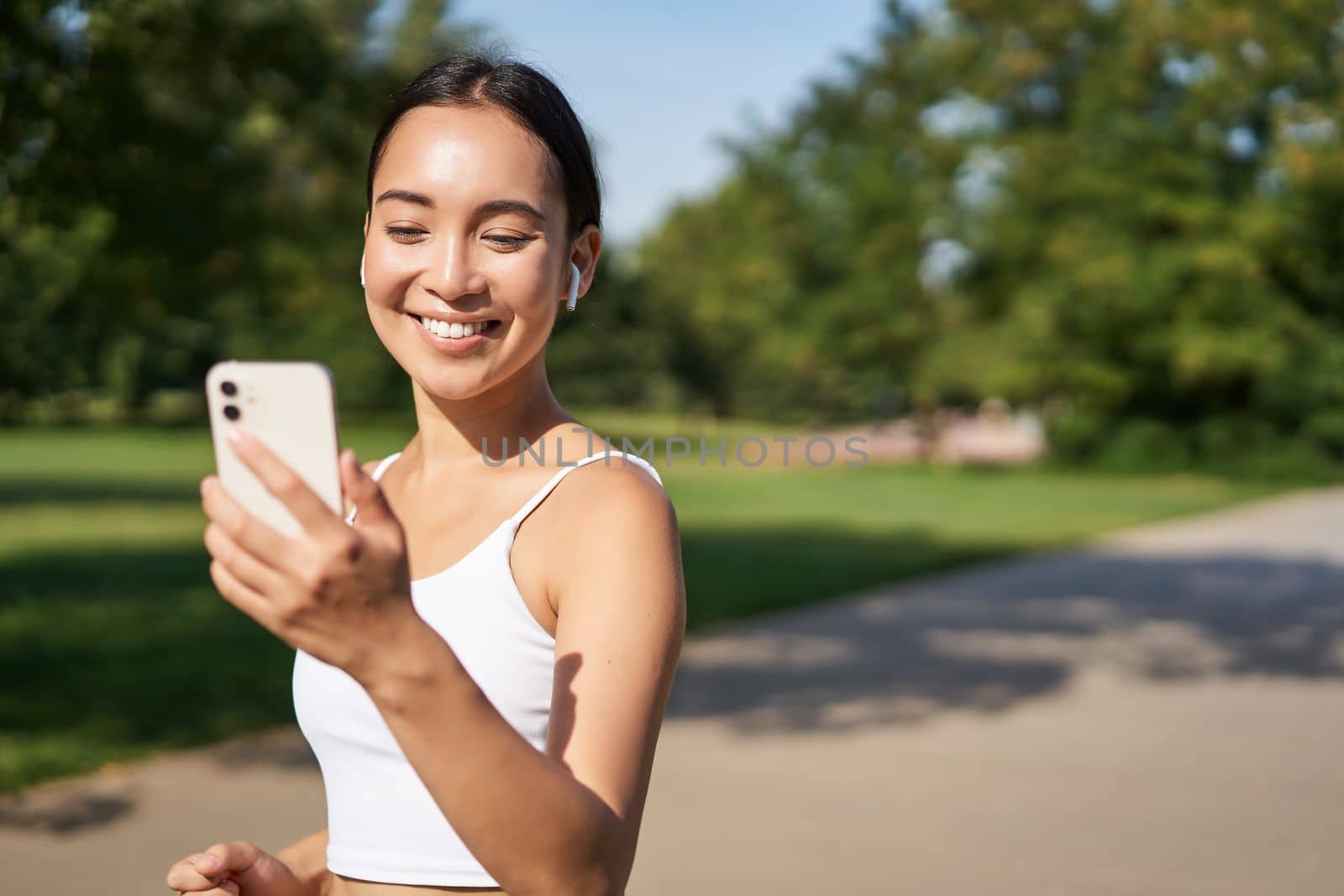 Happy asian fitness girl running and checking her stats, daily goals on smartphone app. Young woman jogging and looking at mobile screen.