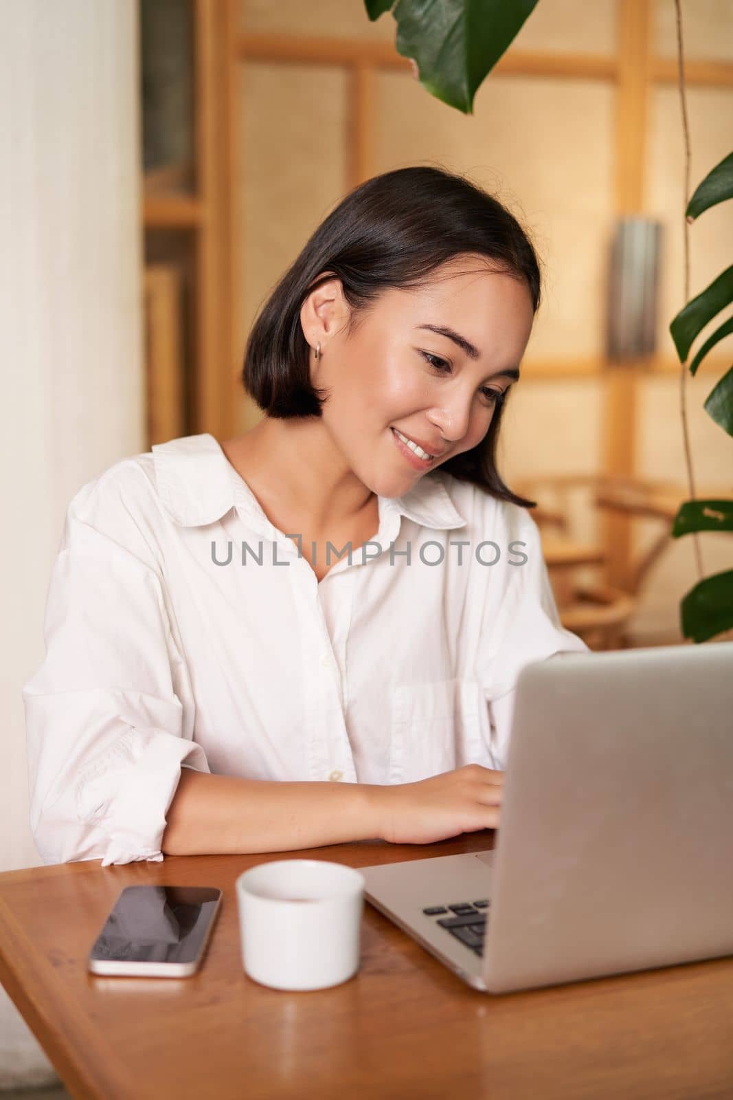 Smiling female manager, freelancer or student sitting with laptop in cafe and working, typing on computer.