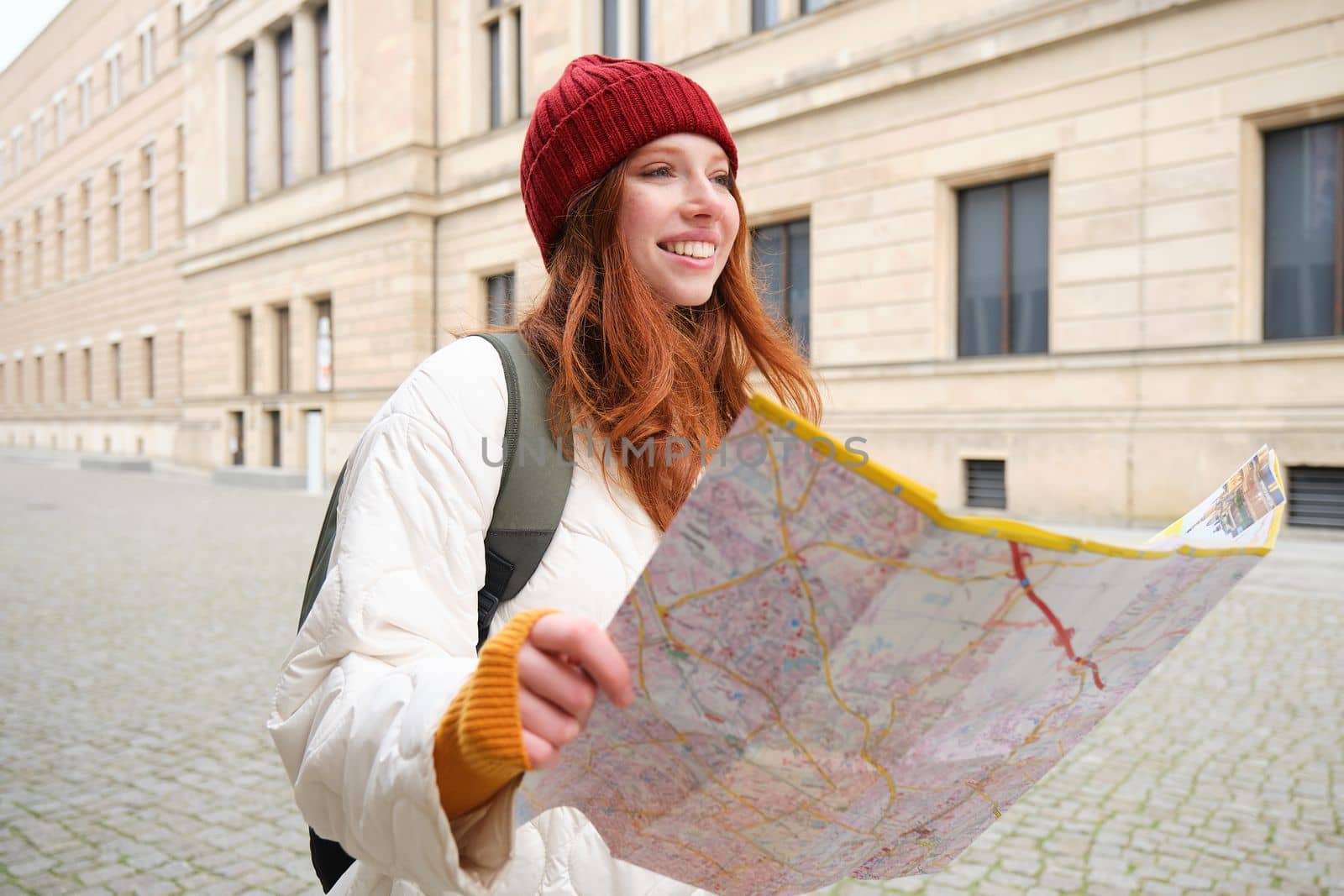 Beautiful redhead woman, tourist with city map, explores sightseeing historical landmark, walking around old town, smiling happily by Benzoix