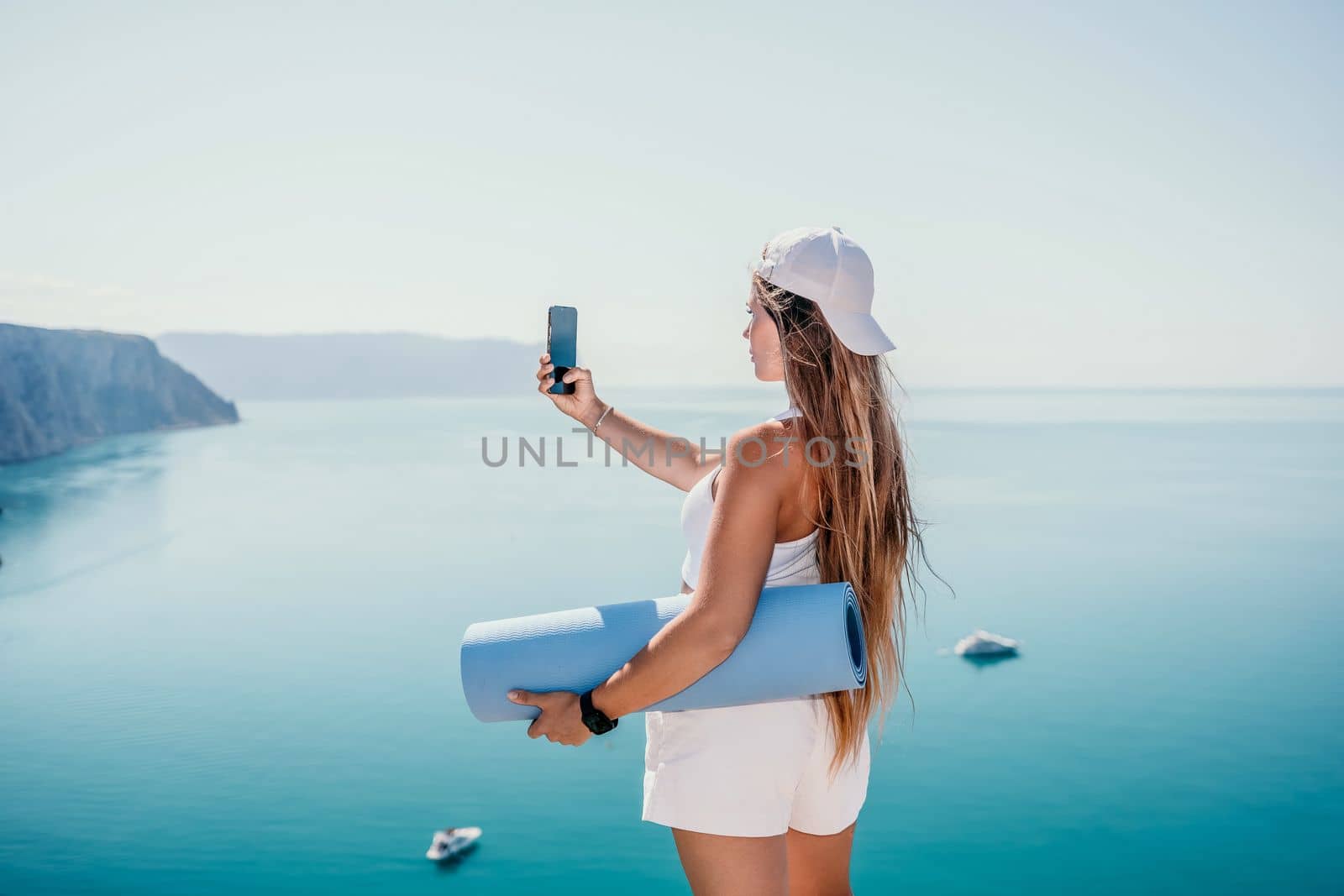 Young woman with black hair, fitness instructor in pink sports leggings and tops, doing pilates on yoga mat with magic pilates ring by the sea on the beach. Female fitness daily yoga concept