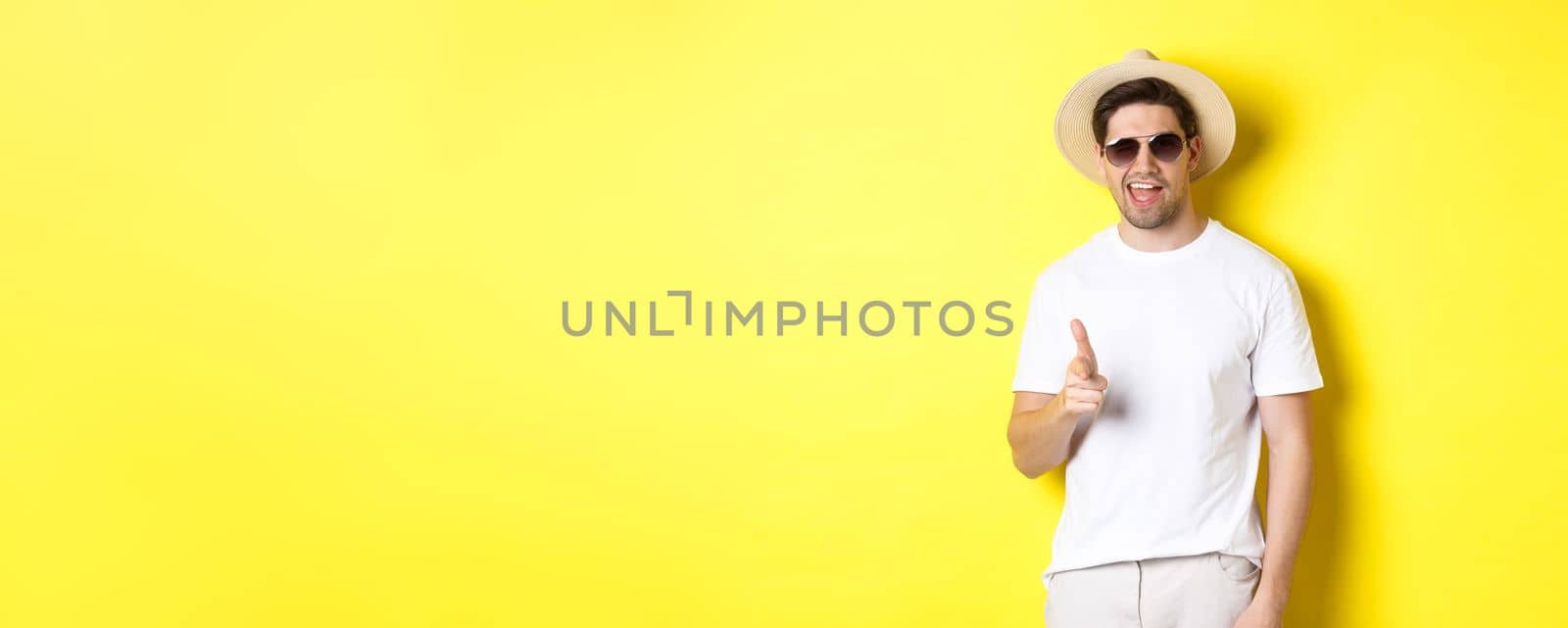 Confident and cheeky guy on vacation flirting with you, pointing finger at camera and winking, wearing summer hat with sunglasses, yellow background by Benzoix